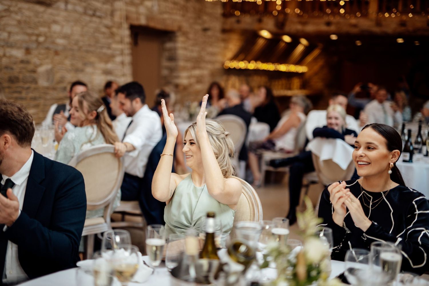 Wedding reception celebration with guests enjoying dinner under ambient lighting in rustic stone venue.