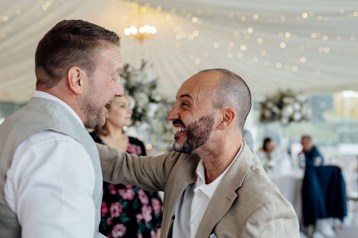 Wedding guests dancing and celebrating under string lights at indoor reception.