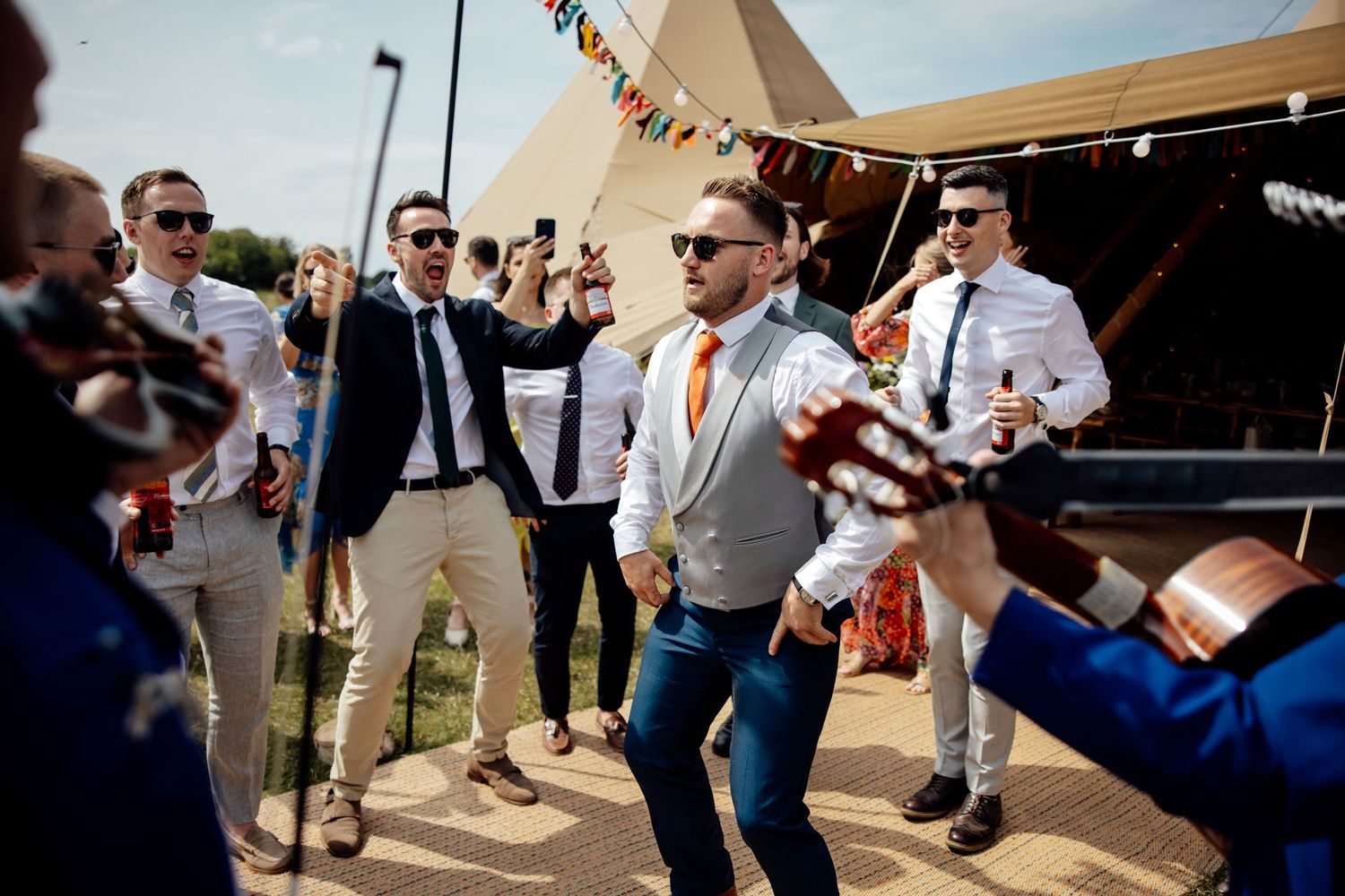 Guests dancing and celebrating at an outdoor wedding reception under a tent.