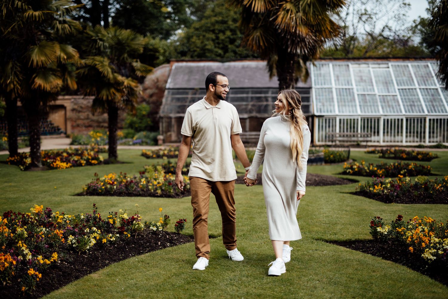 A couple strolls hand in hand through a beautiful garden with blooming flowers.