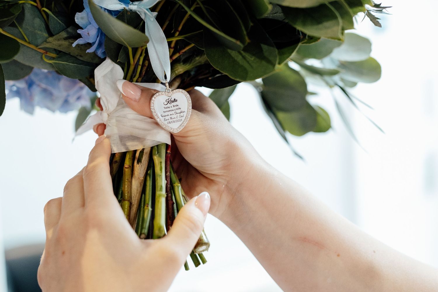 Close-up of hands attaching a sentimental charm to a wedding bouquet.
