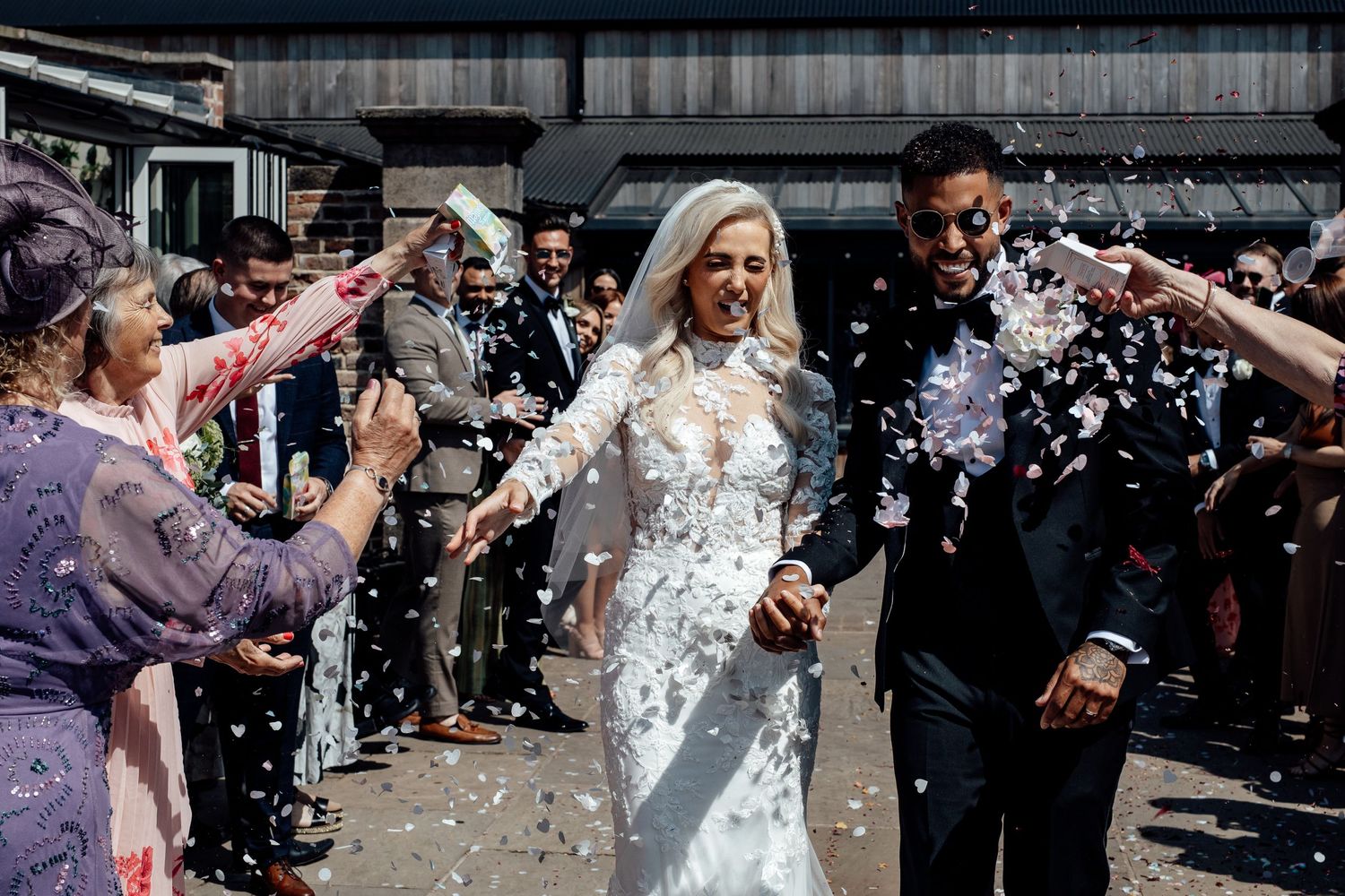 Wedding guests shower the newlyweds with confetti during an outdoor celebration.