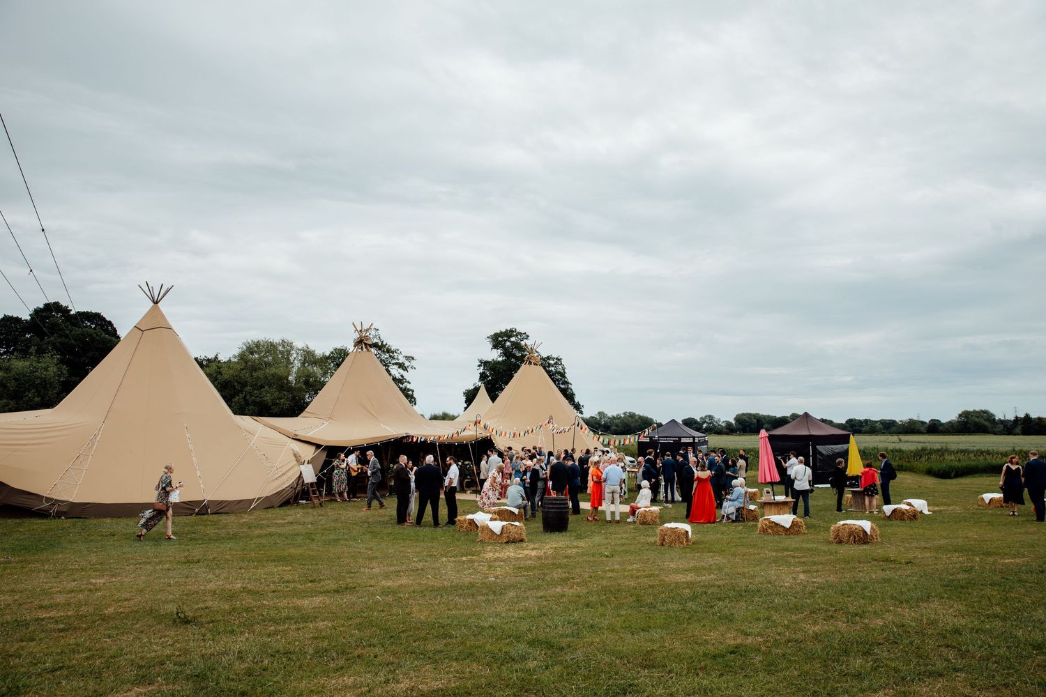Large tipi-style tents set up in a field for an outdoor wedding reception.