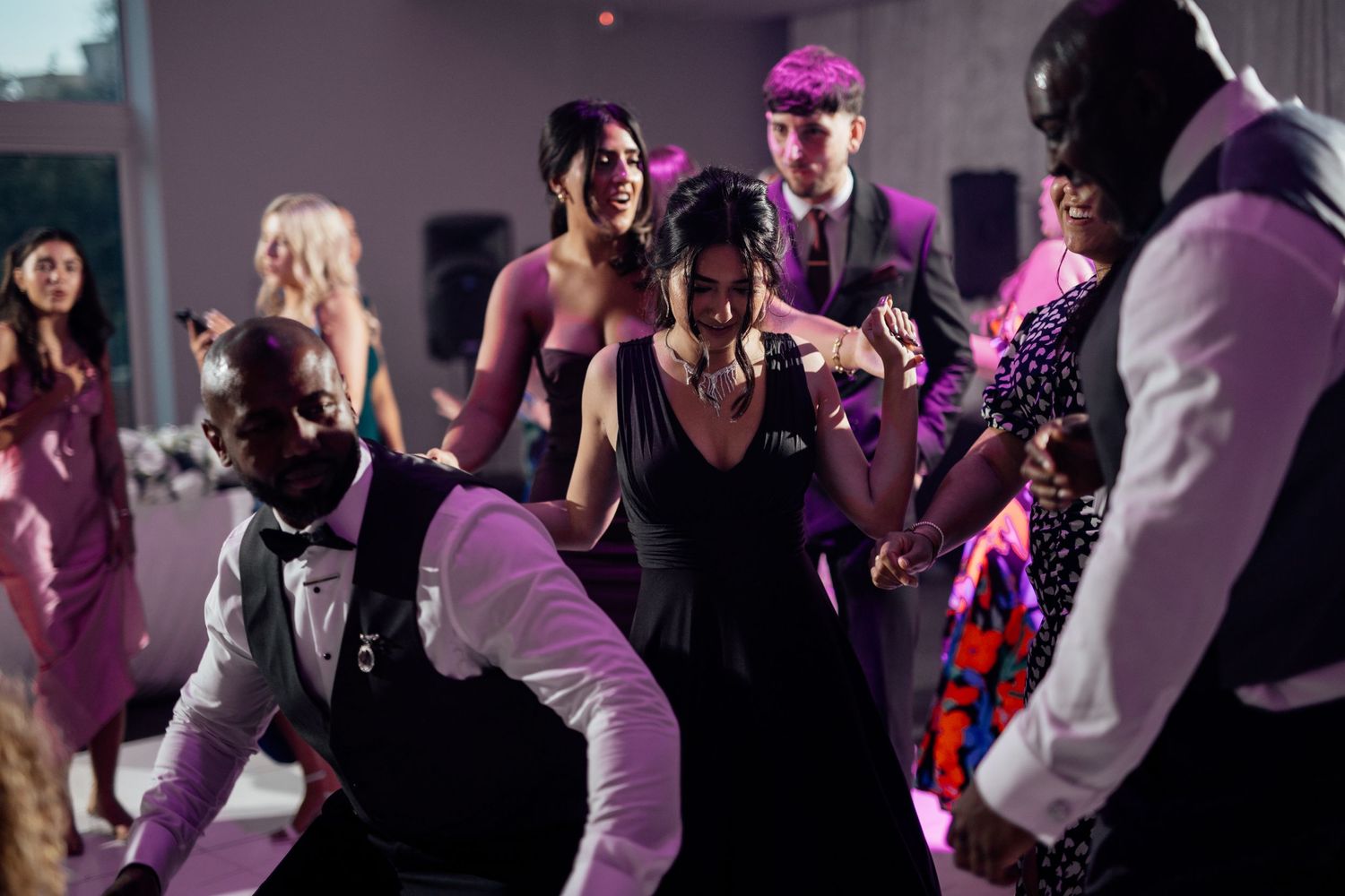 Wedding reception dance floor with purple lighting and guests dancing.