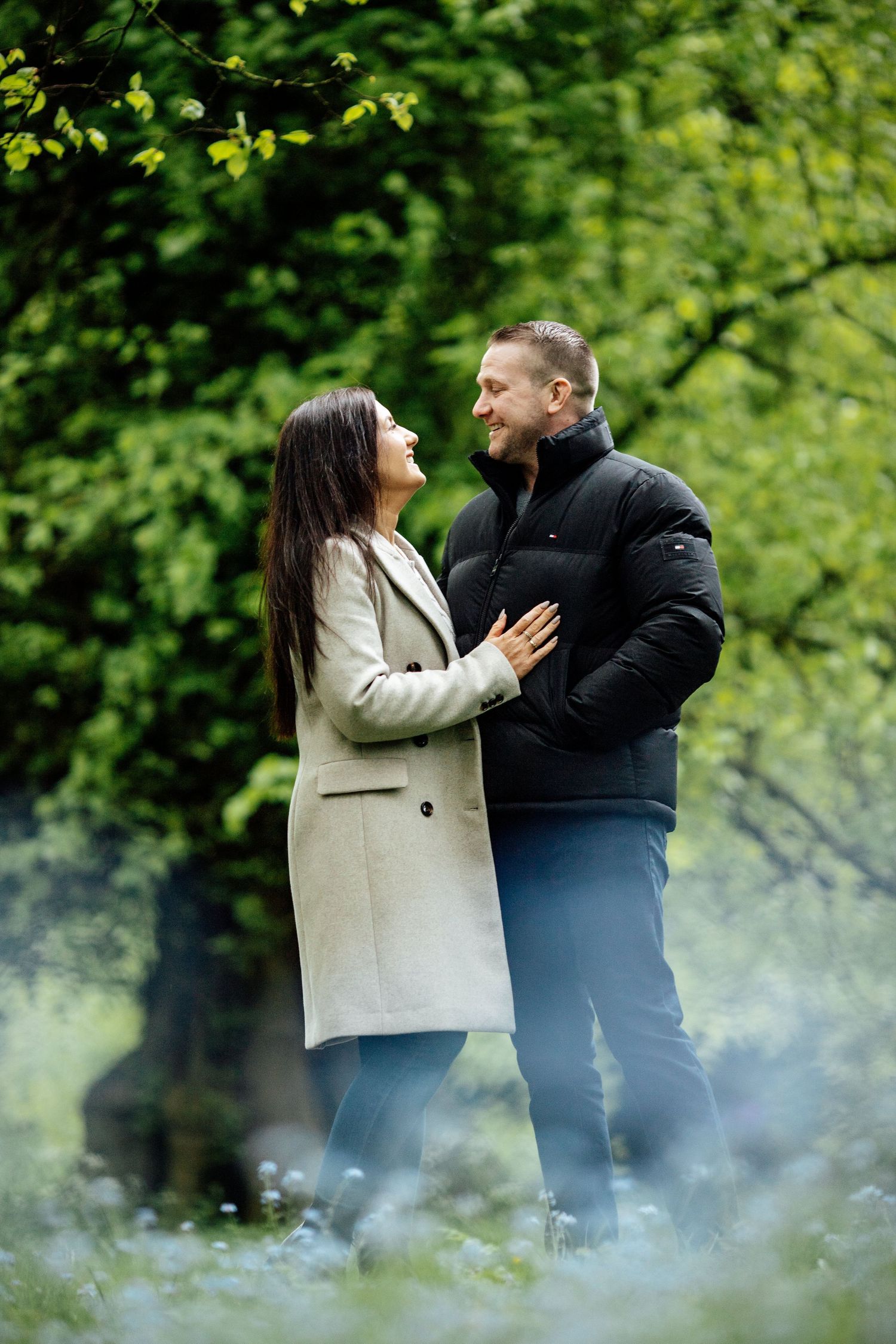 Two people share a tender moment against a backdrop of green foliage and misty atmosphere.