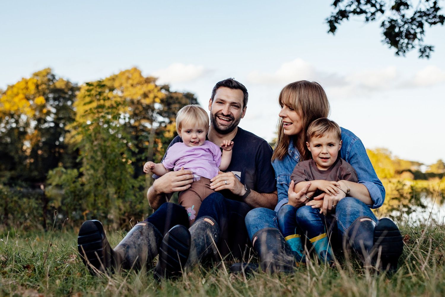 Family relaxing together on grassy hill during sunset photo session.