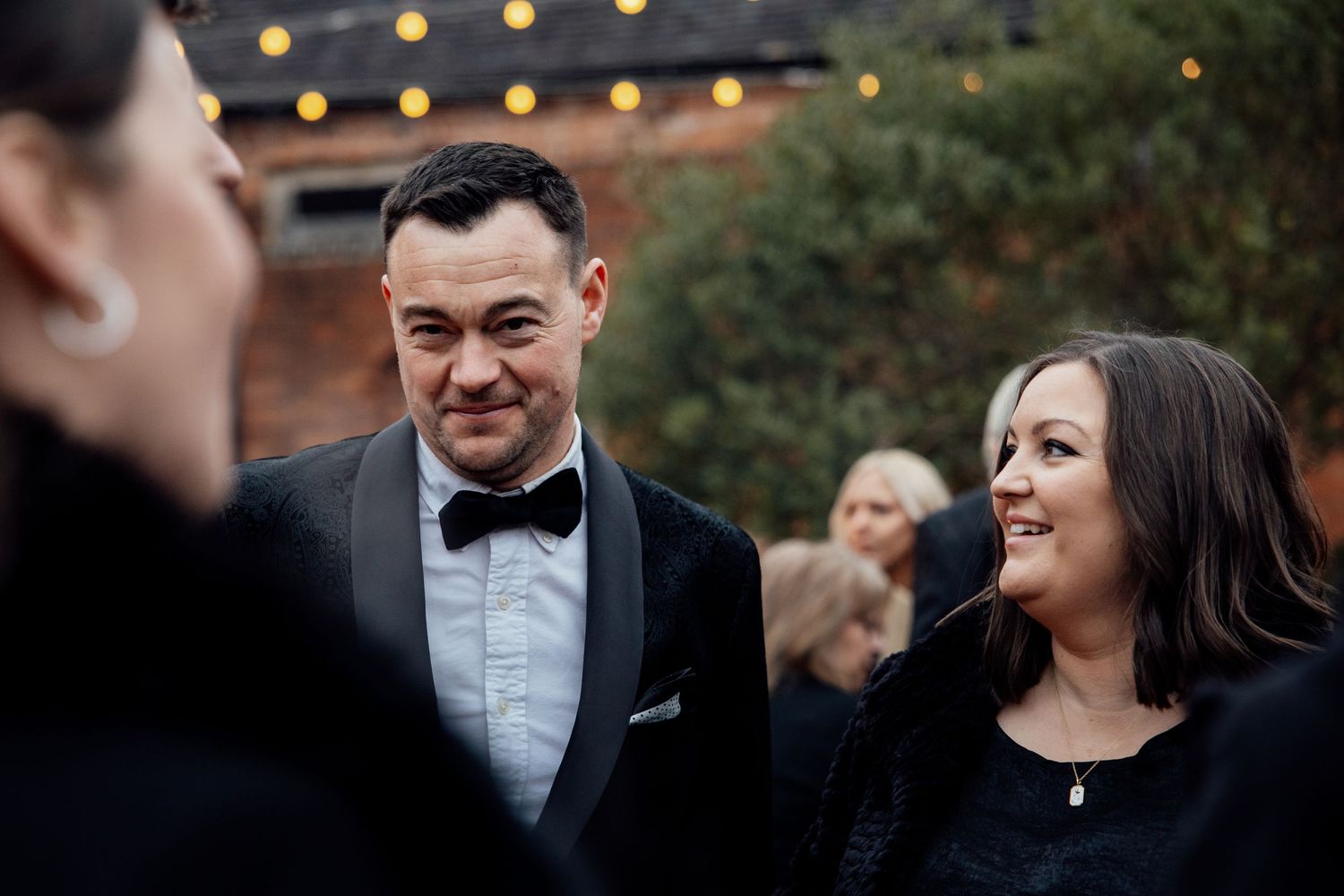 Wedding guests mingling and laughing during an outdoor evening reception.