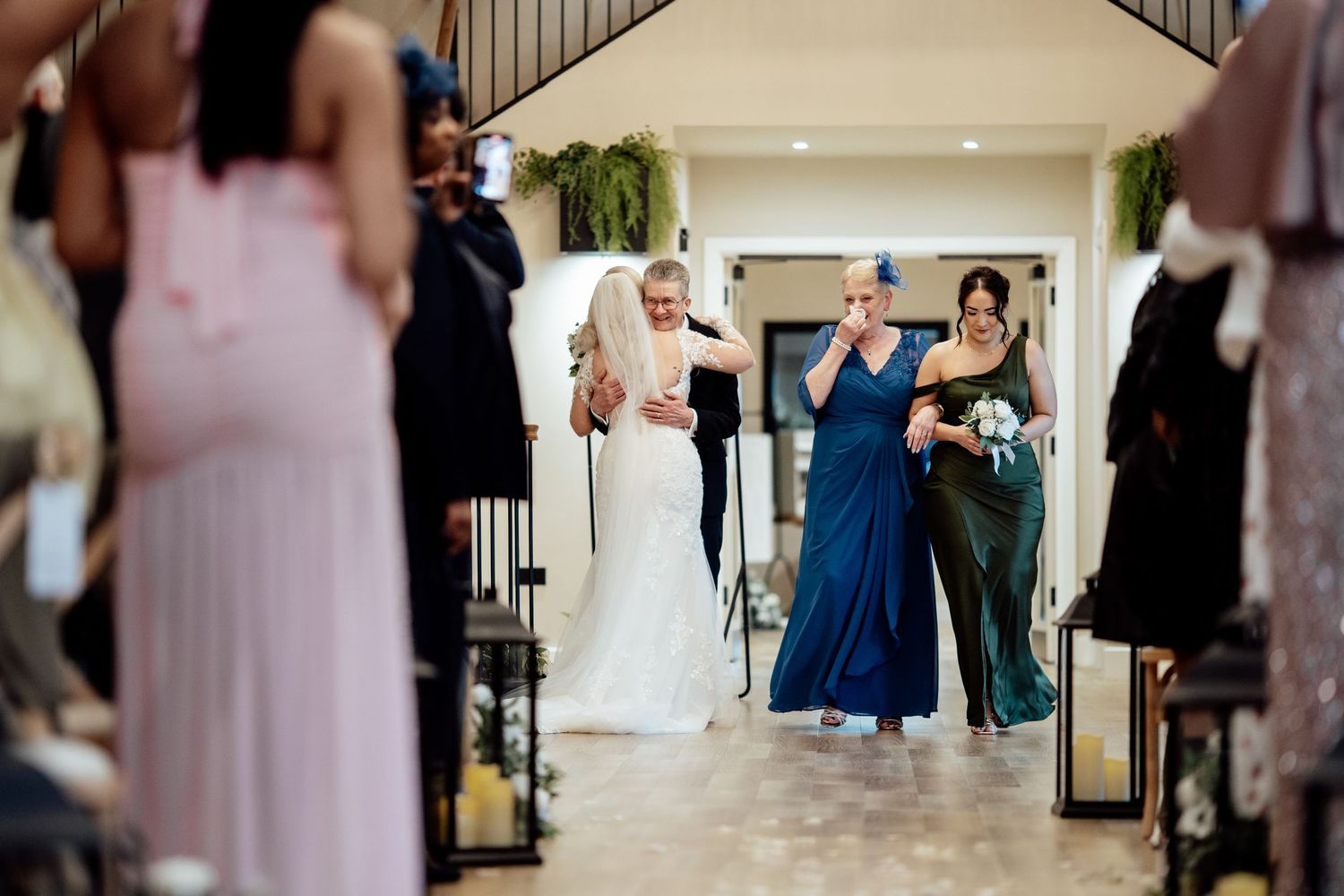 Bride walking down the aisle escorted by two women in a bright elegant wedding ceremony venue.