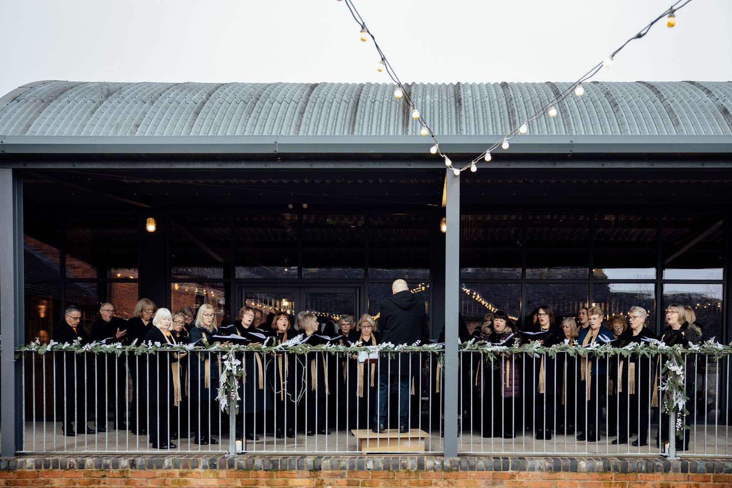Wedding guests in formal attire gathered on a balcony with string lights.