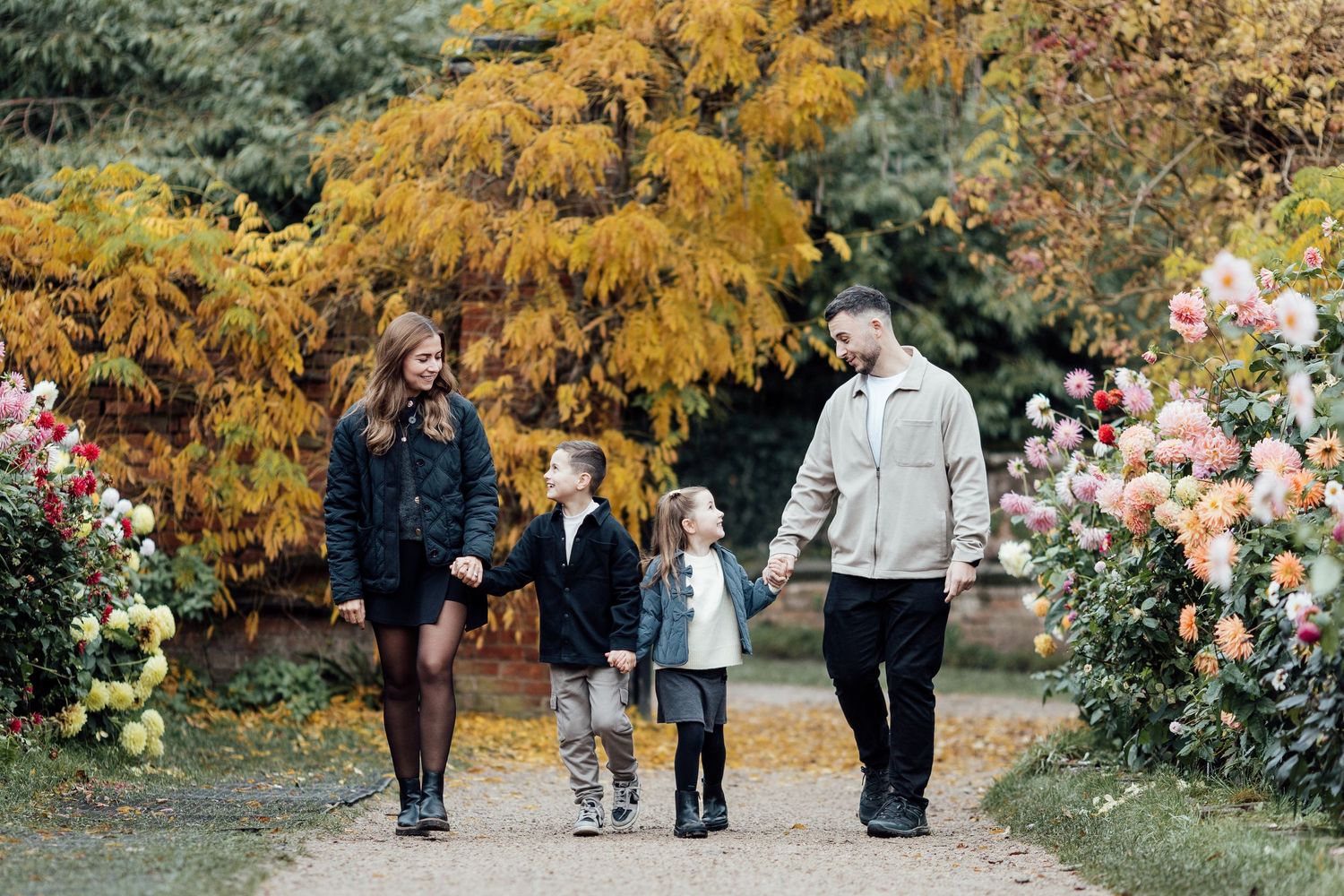 People walking through a garden path with yellow autumn trees in background.