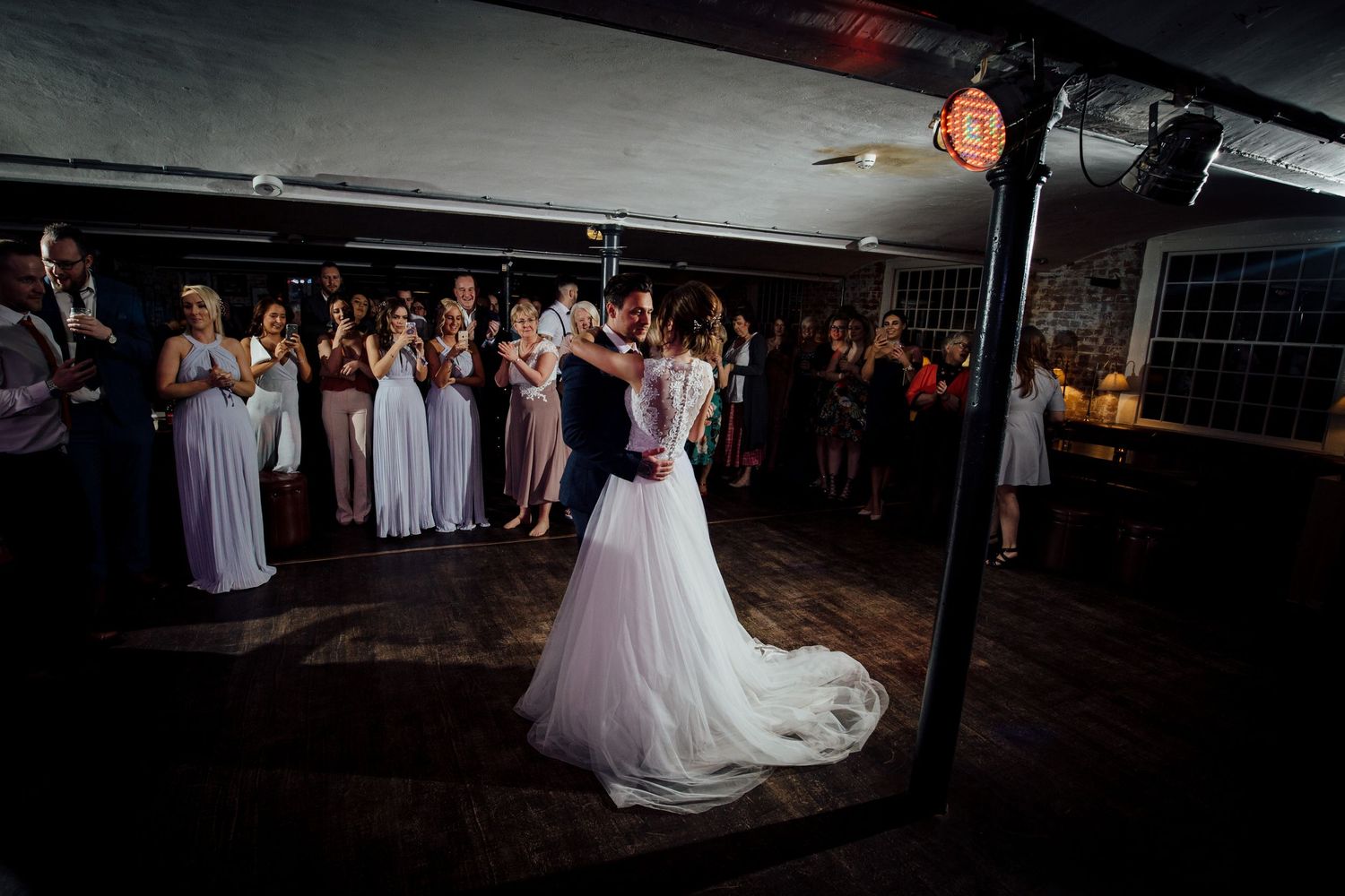 Wedding reception dance floor filled with guests celebrating in dimly lit venue.