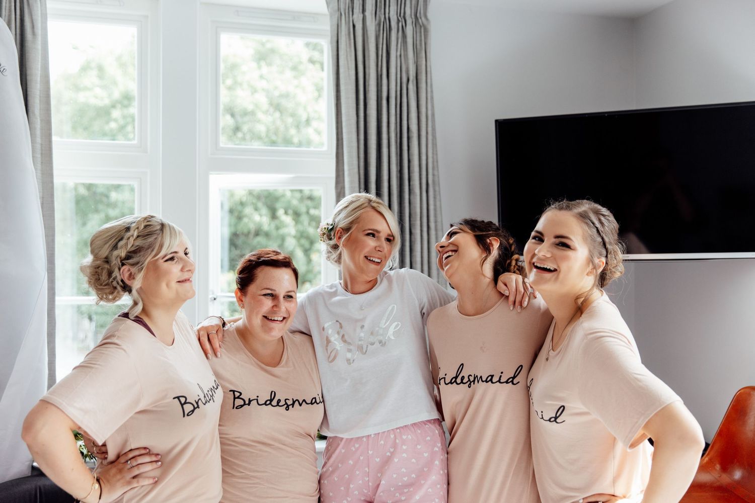 Group wearing matching robes pose together in a bright white room during wedding preparations.