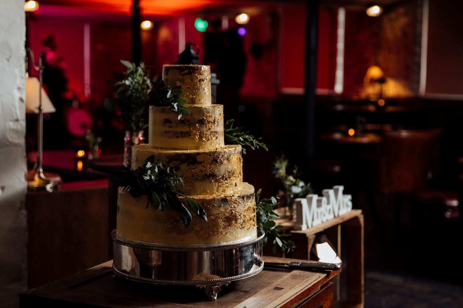Elegant tiered wedding cake displayed in dimly lit reception venue.