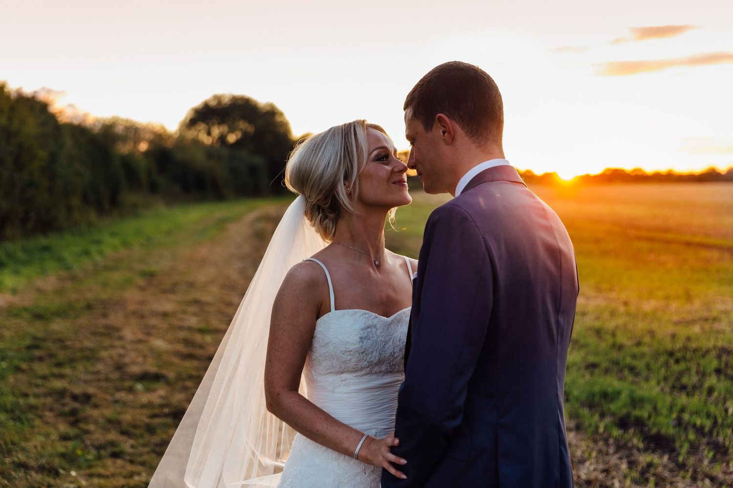 Couple shares an intimate moment against a warm sunset backdrop in a countryside setting.