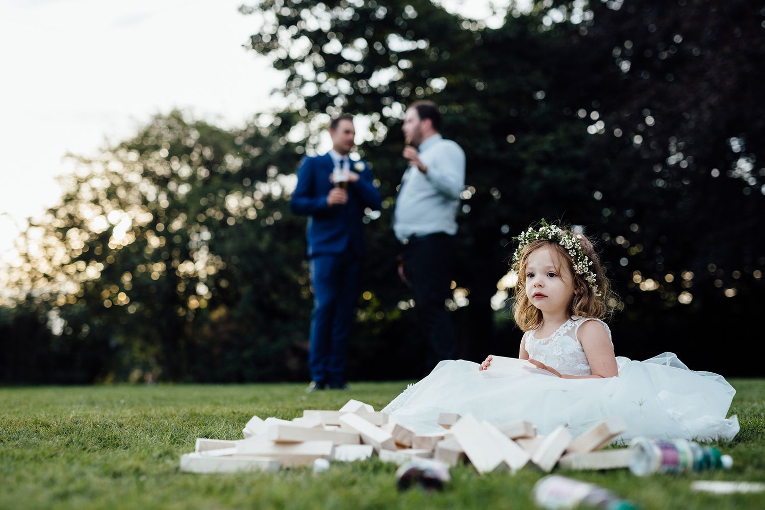 A romantic outdoor wedding celebration with guests gathered on a grassy lawn at sunset.