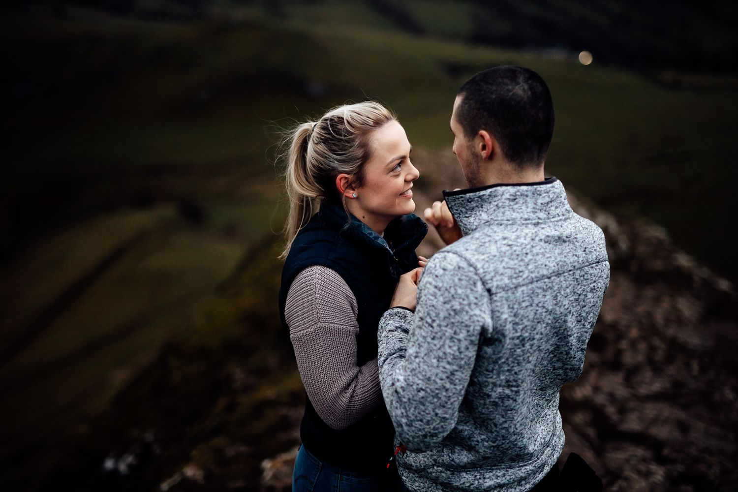 A romantic couple embraces against a moody dark background in an intimate outdoor photoshoot.