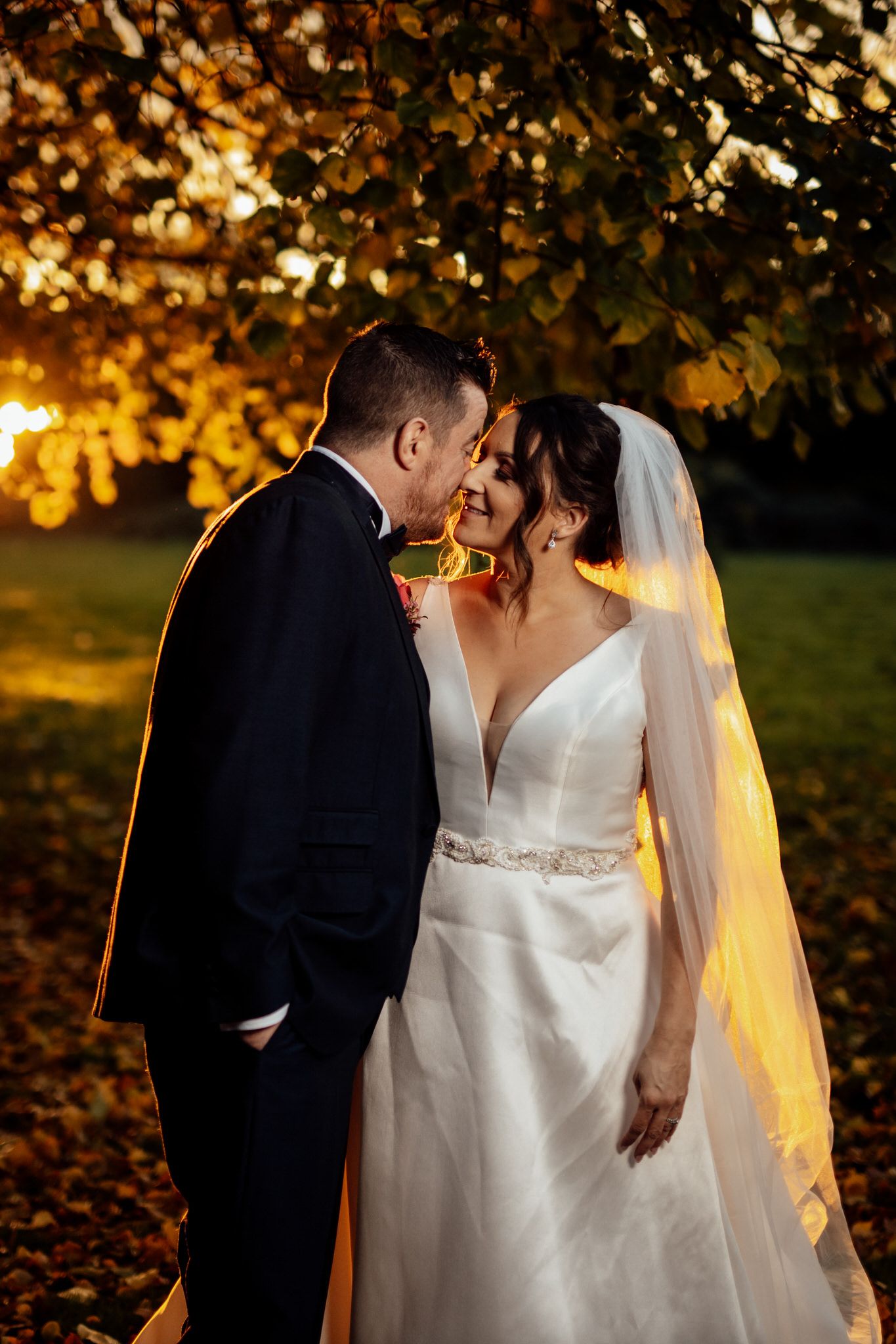 Romantic autumn wedding portraits with golden sunlight filtering through fall foliage.