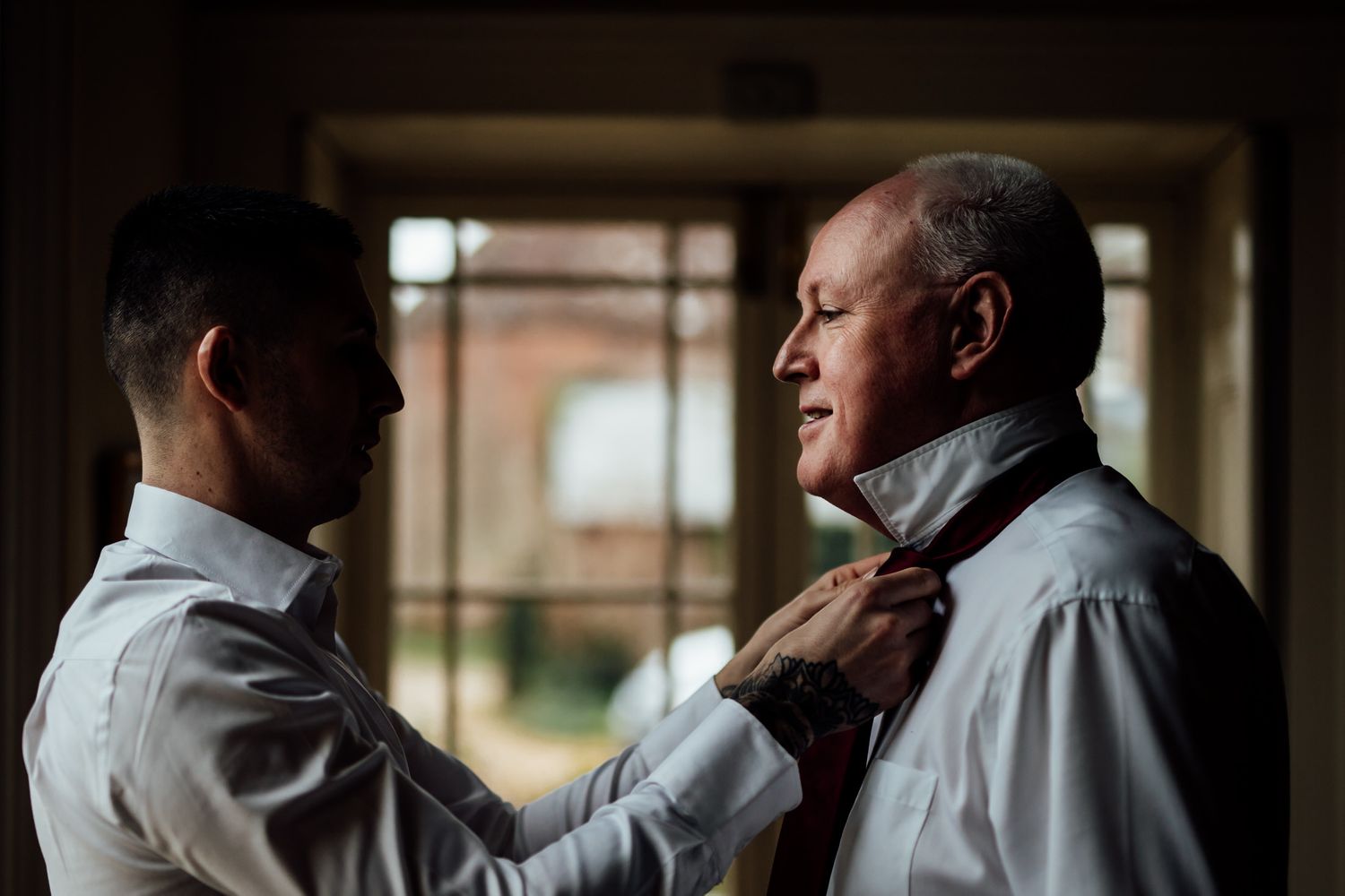 Men in formal attire getting ready in a dimly lit room before a special event.