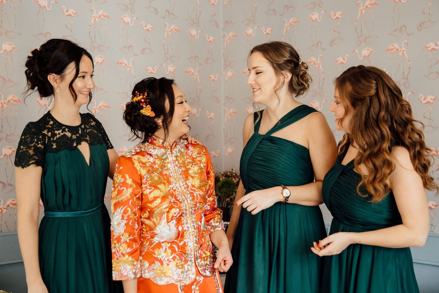 Bridesmaids in emerald green dresses stand with bride in traditional Asian attire.