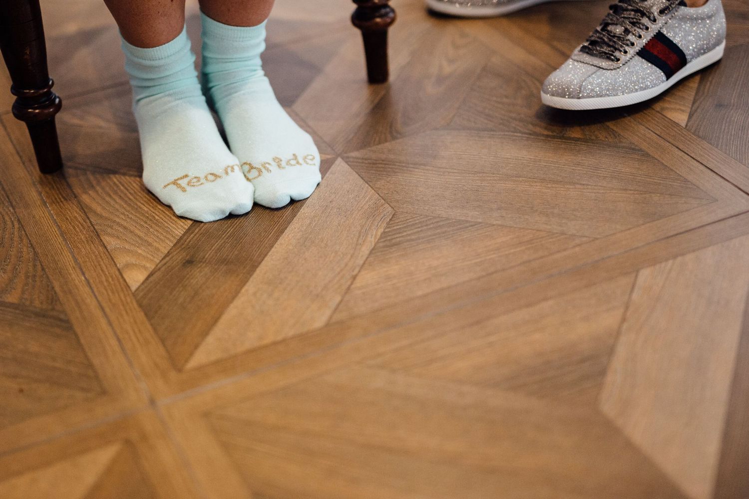 Close-up of mint colored socks and dress shoes on a herringbone wooden floor.