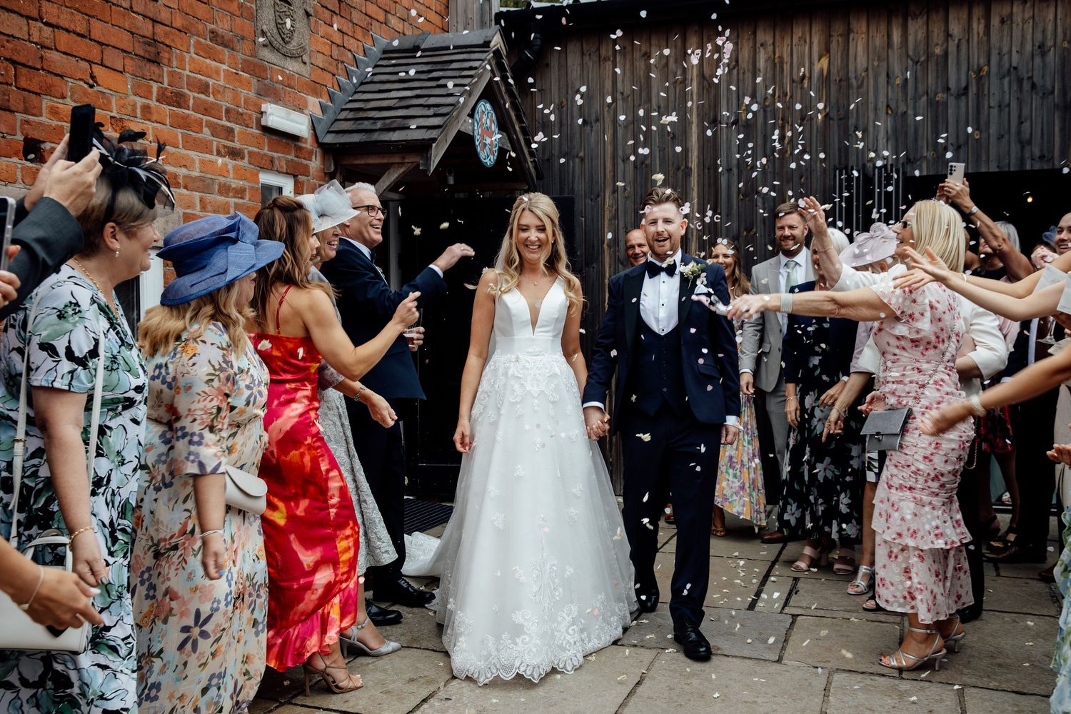 Wedding guests celebrate with confetti outside a rustic brick venue.
