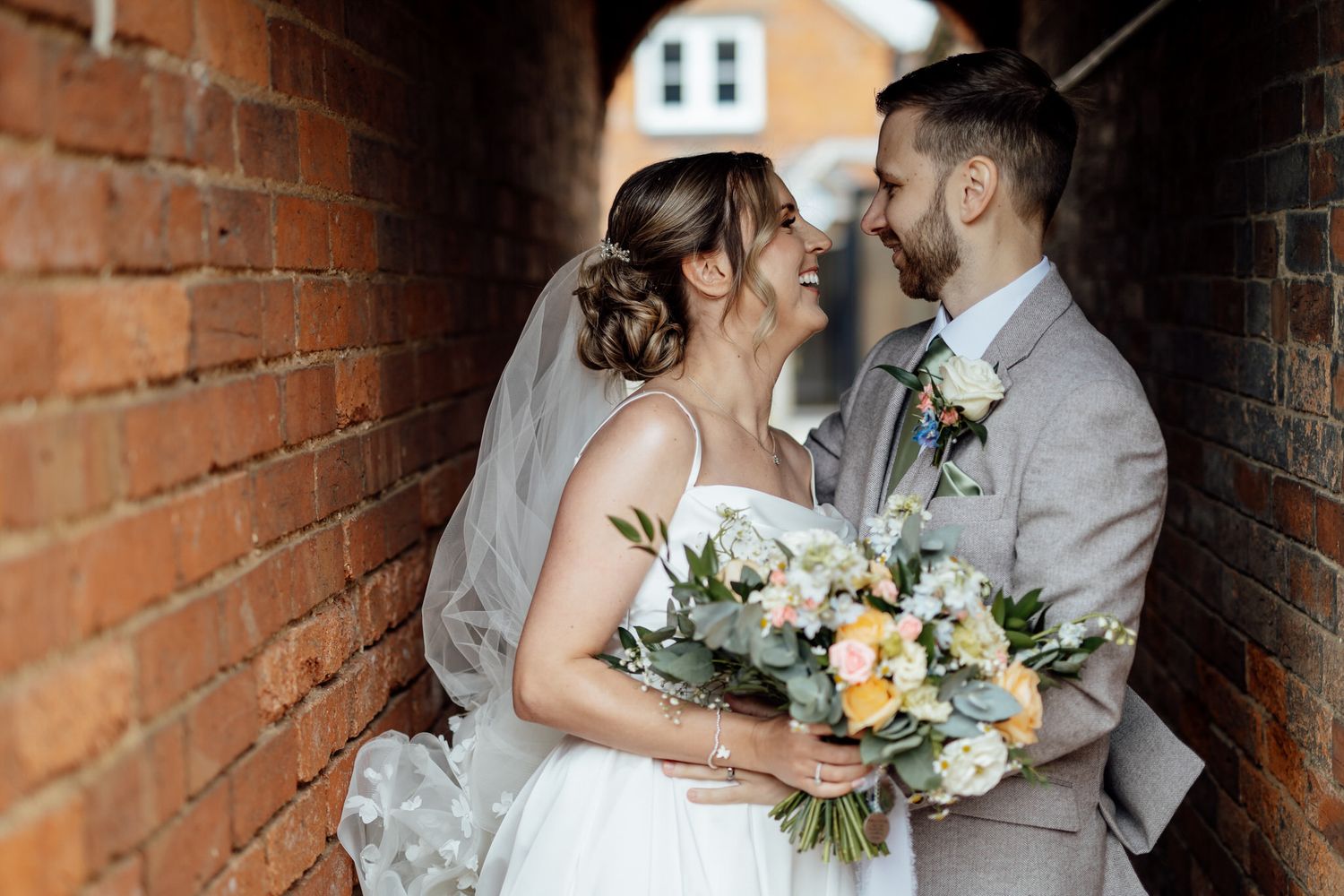 Romantic wedding couple moment against brick wall with floral bouquet.