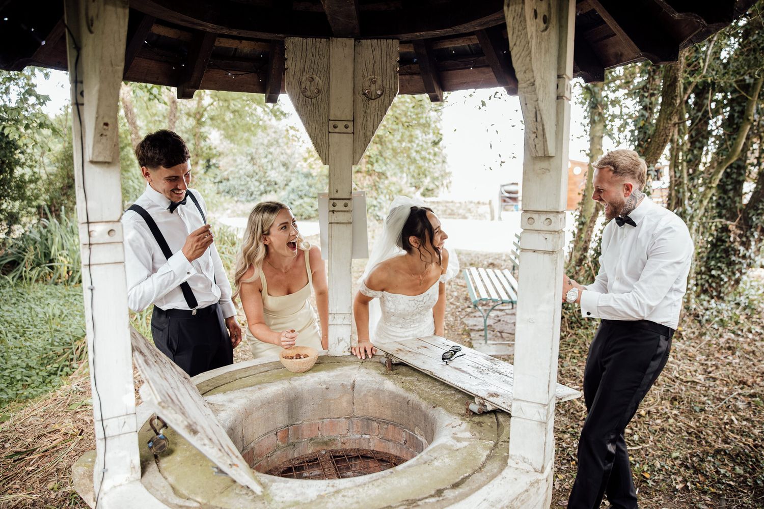 Wedding party gathered around rustic gazebo for casual photos.