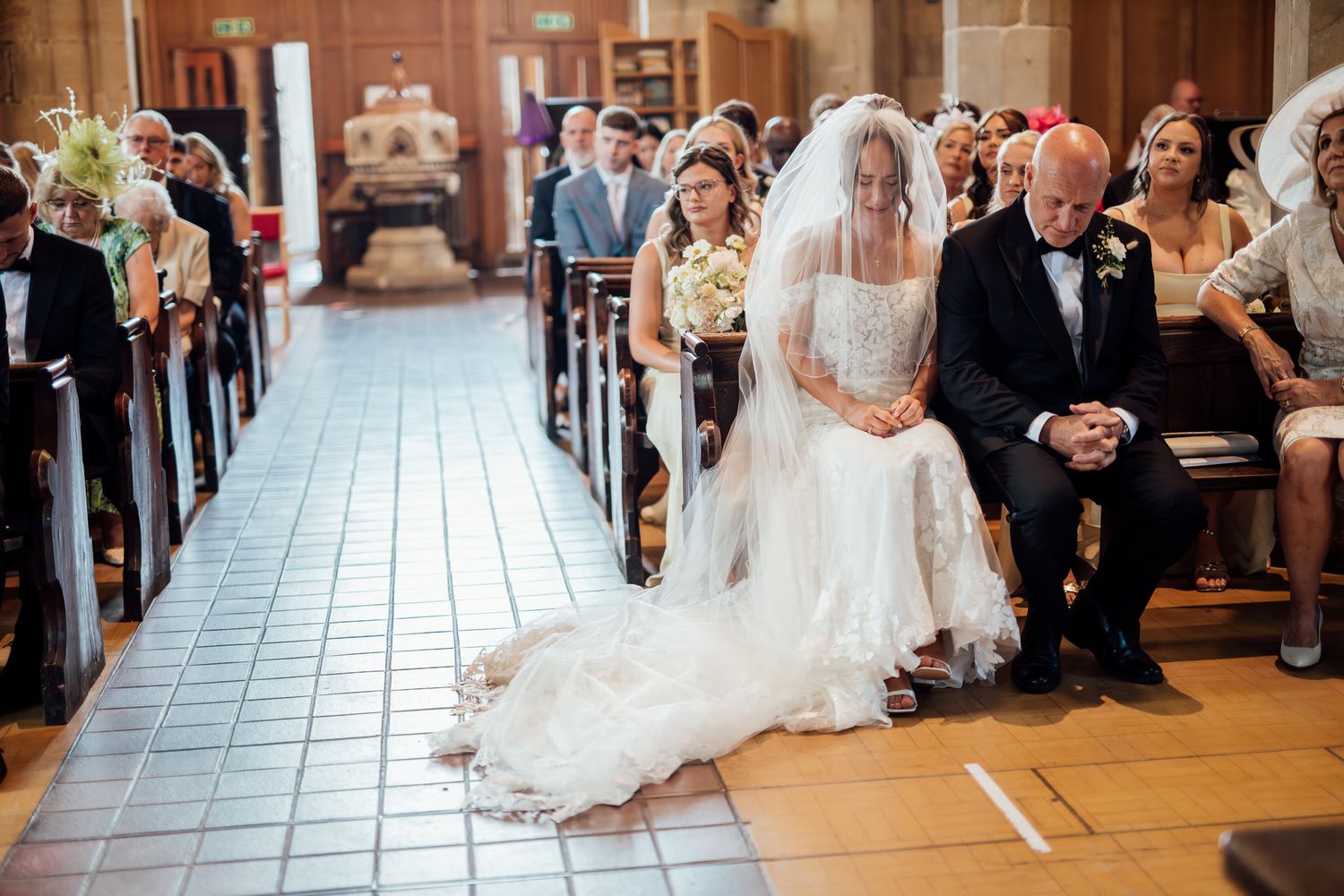 Wedding ceremony guests seated in rows inside an elegant church with white decor and tiled floors.