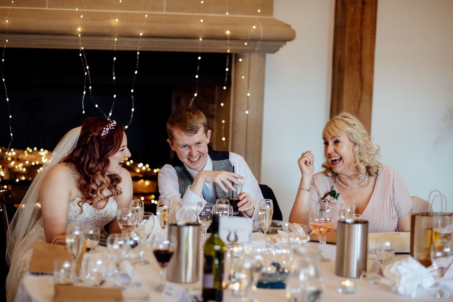 Wedding guests seated at elegant tables with string lights and decorations during an indoor reception celebration.