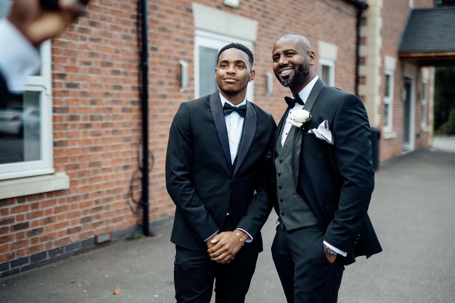 Groomsmen share laughs outside brick venue before ceremony.