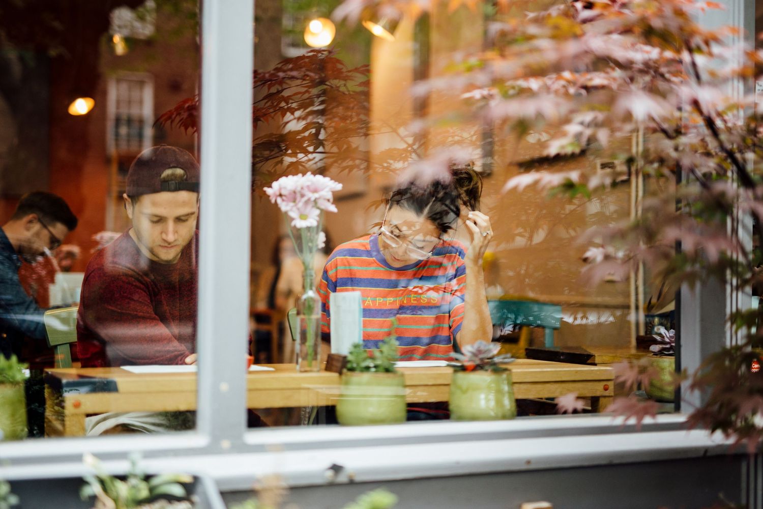 Couple sharing intimate moments in a warmly lit cafe with string lights and window reflections.