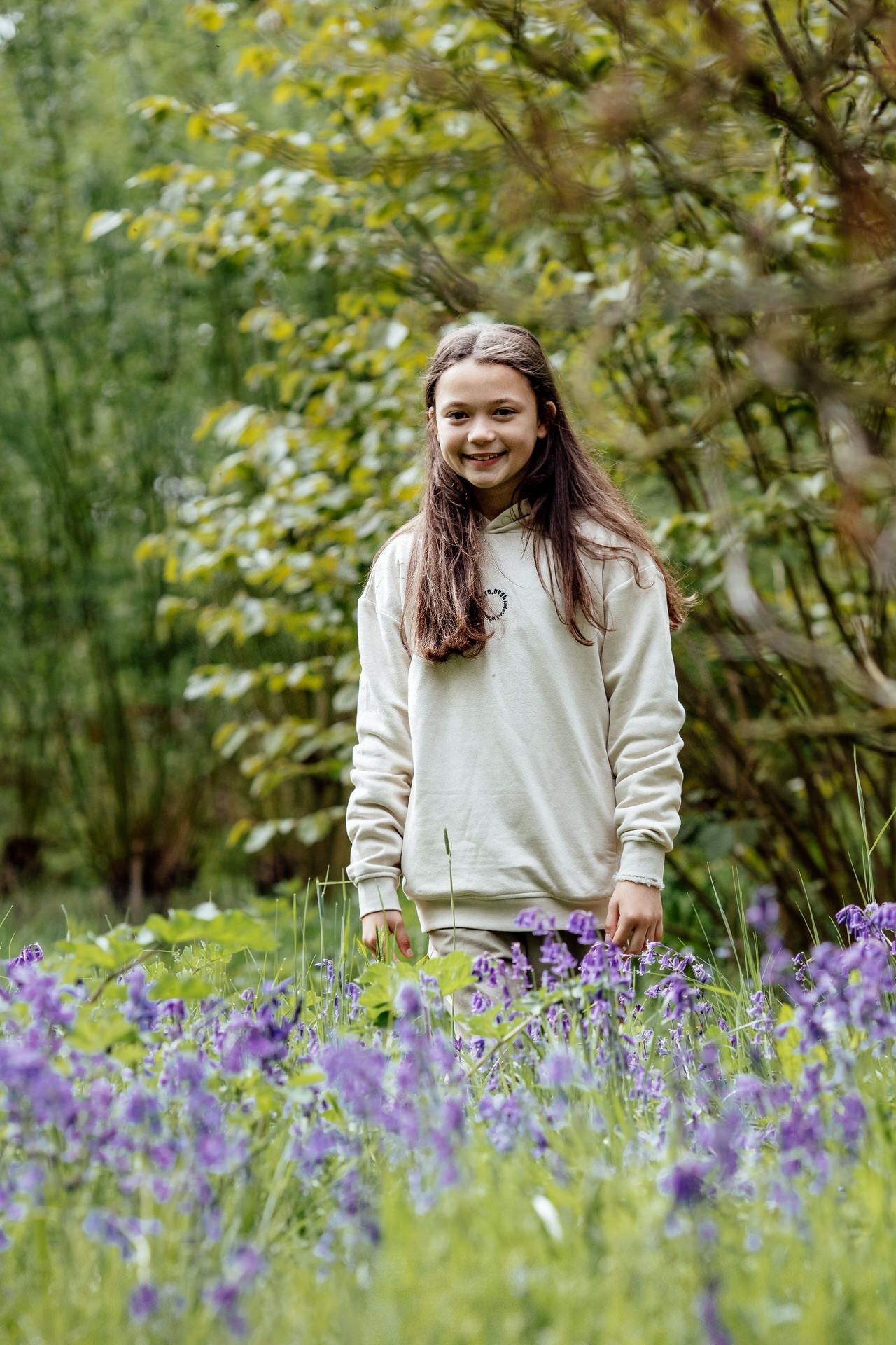 A person in a cream sweater stands among vibrant purple bluebells in a spring garden.