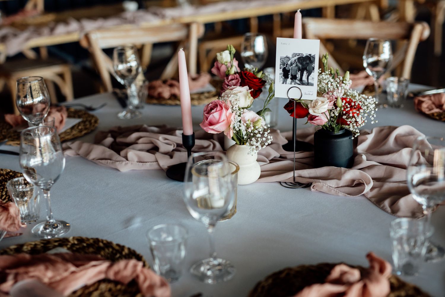 Close-up of floral centerpiece with pink flowers and candles on rustic table.