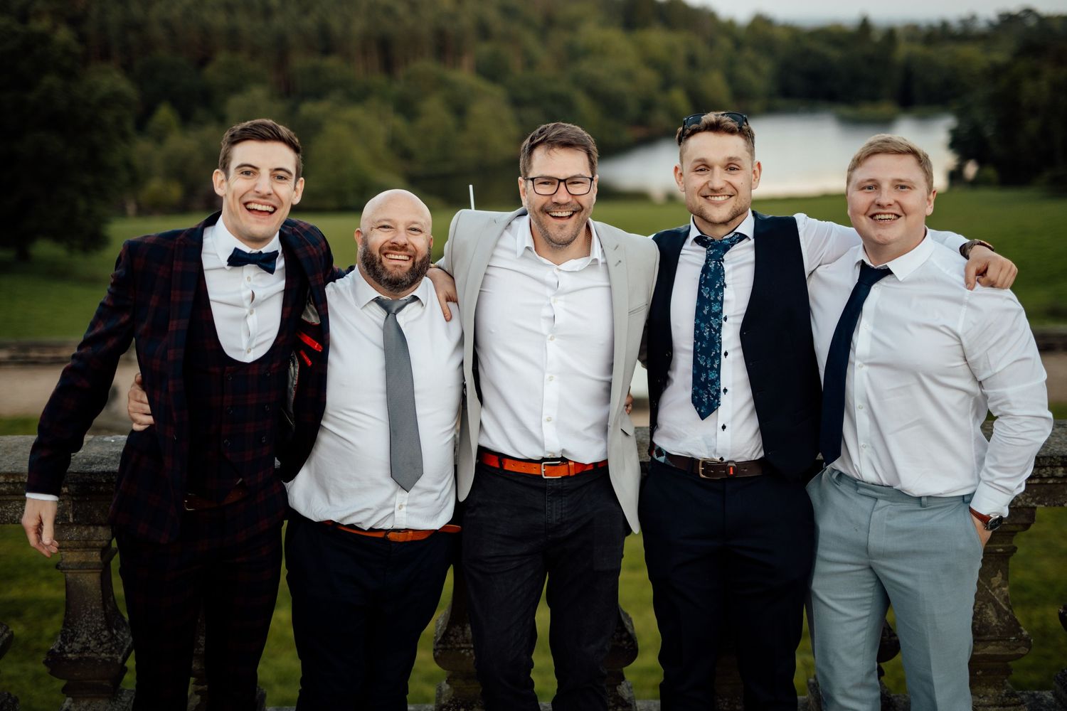 Groomsmen in formal attire pose together outdoors for wedding photos.