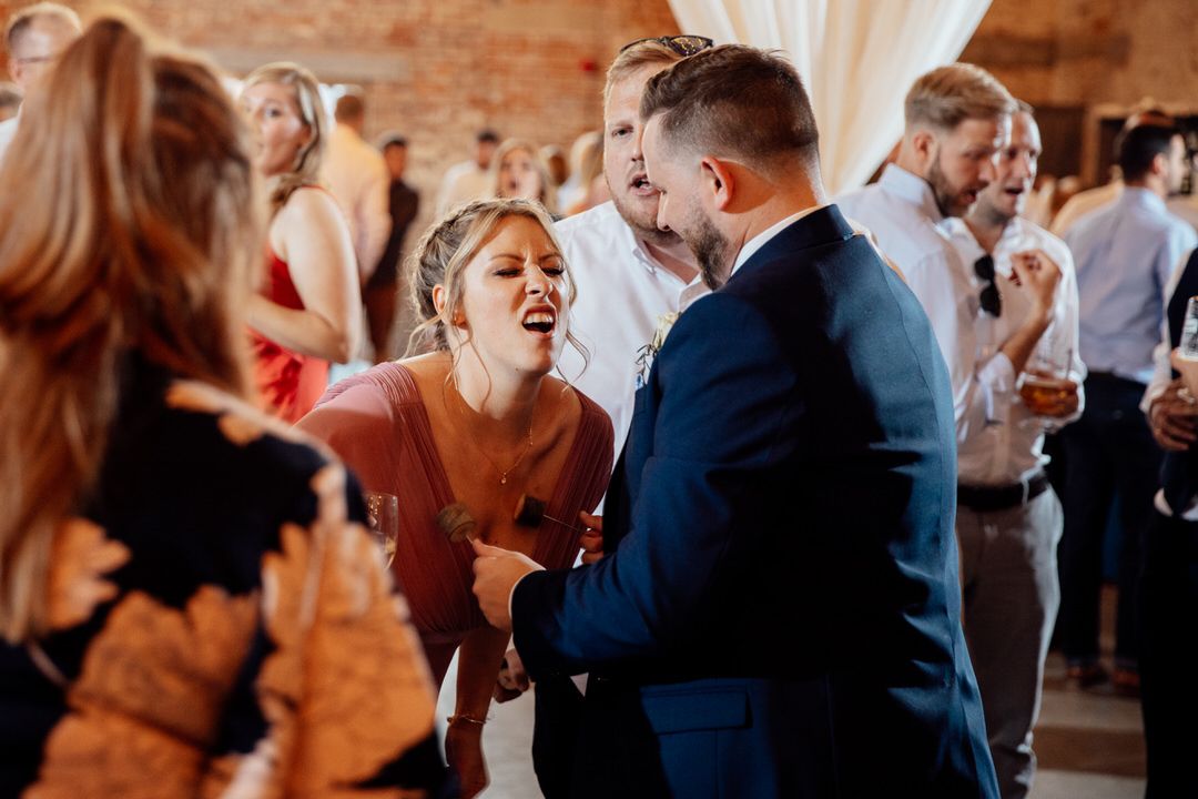 Wedding guests dance and celebrate at reception in warm-lit rustic venue.