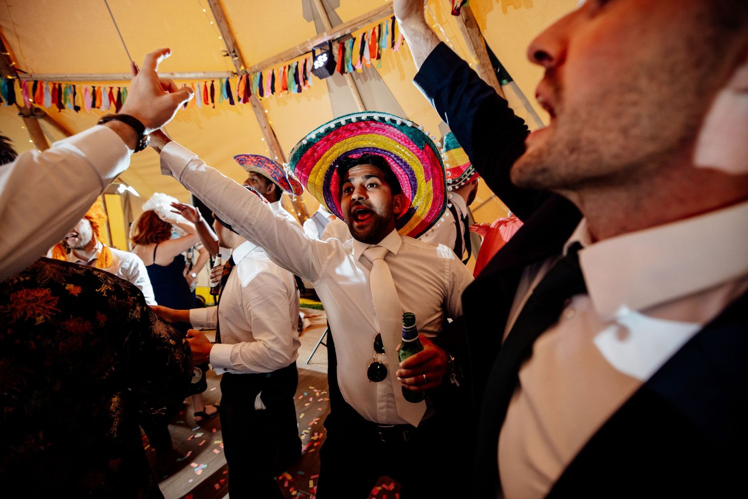 Festive wedding reception under tent with colorful bunting decorations and dancing guests.