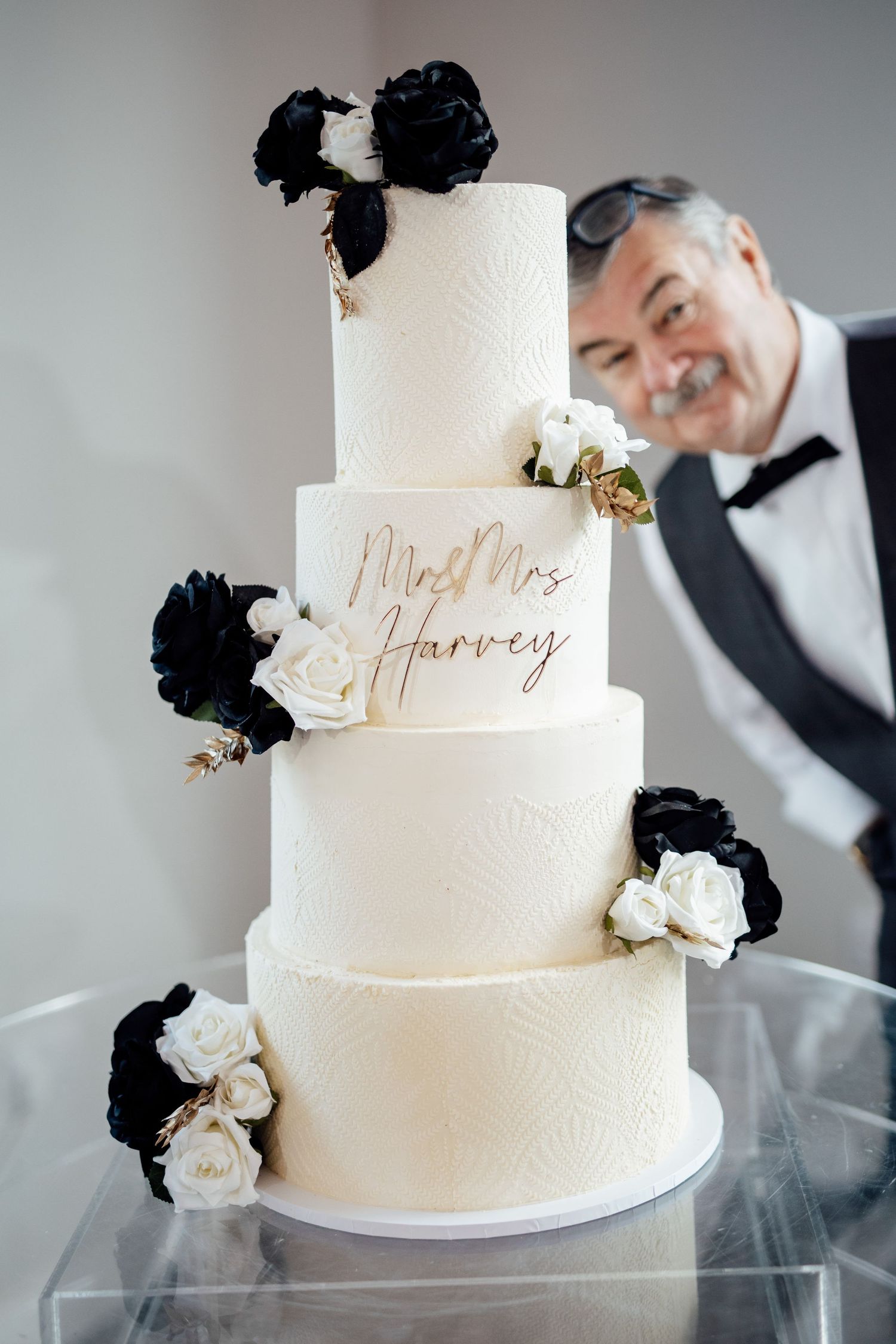 Elegant white wedding cake with black and white floral decorations and gold script text.