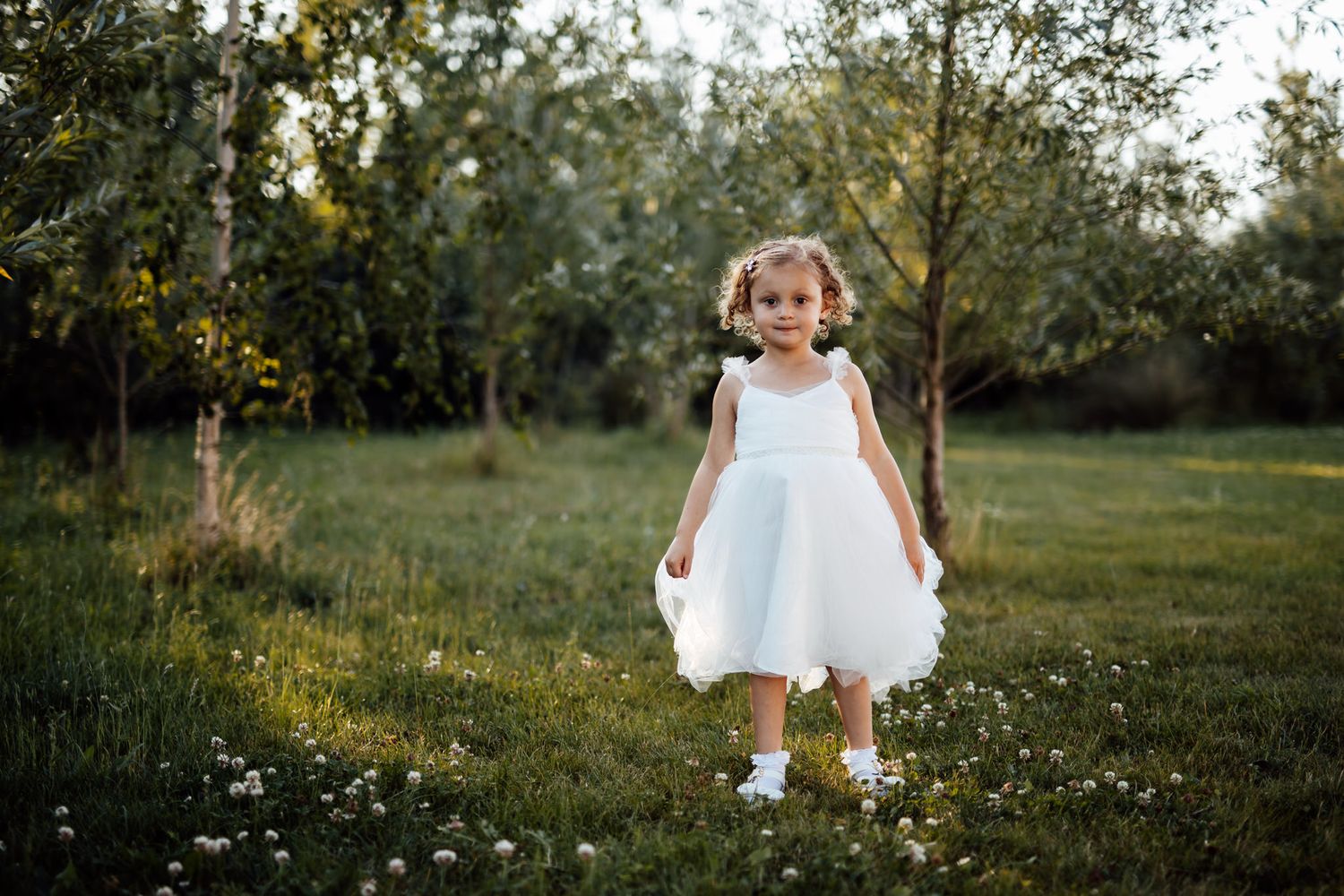 White dress flowing in outdoor garden setting with wildflowers and natural lighting.
