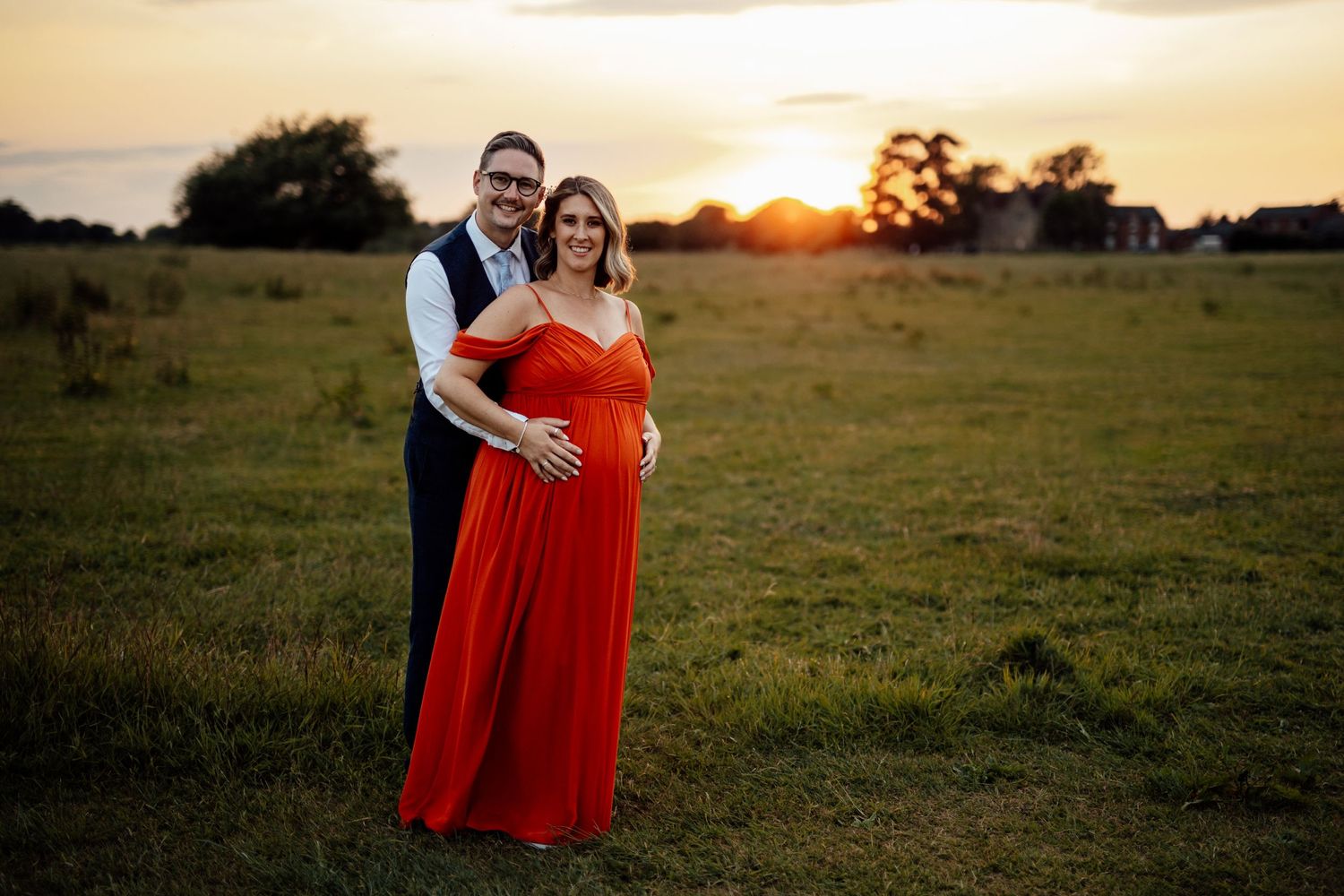 A couple stands together in a field during golden hour sunset.