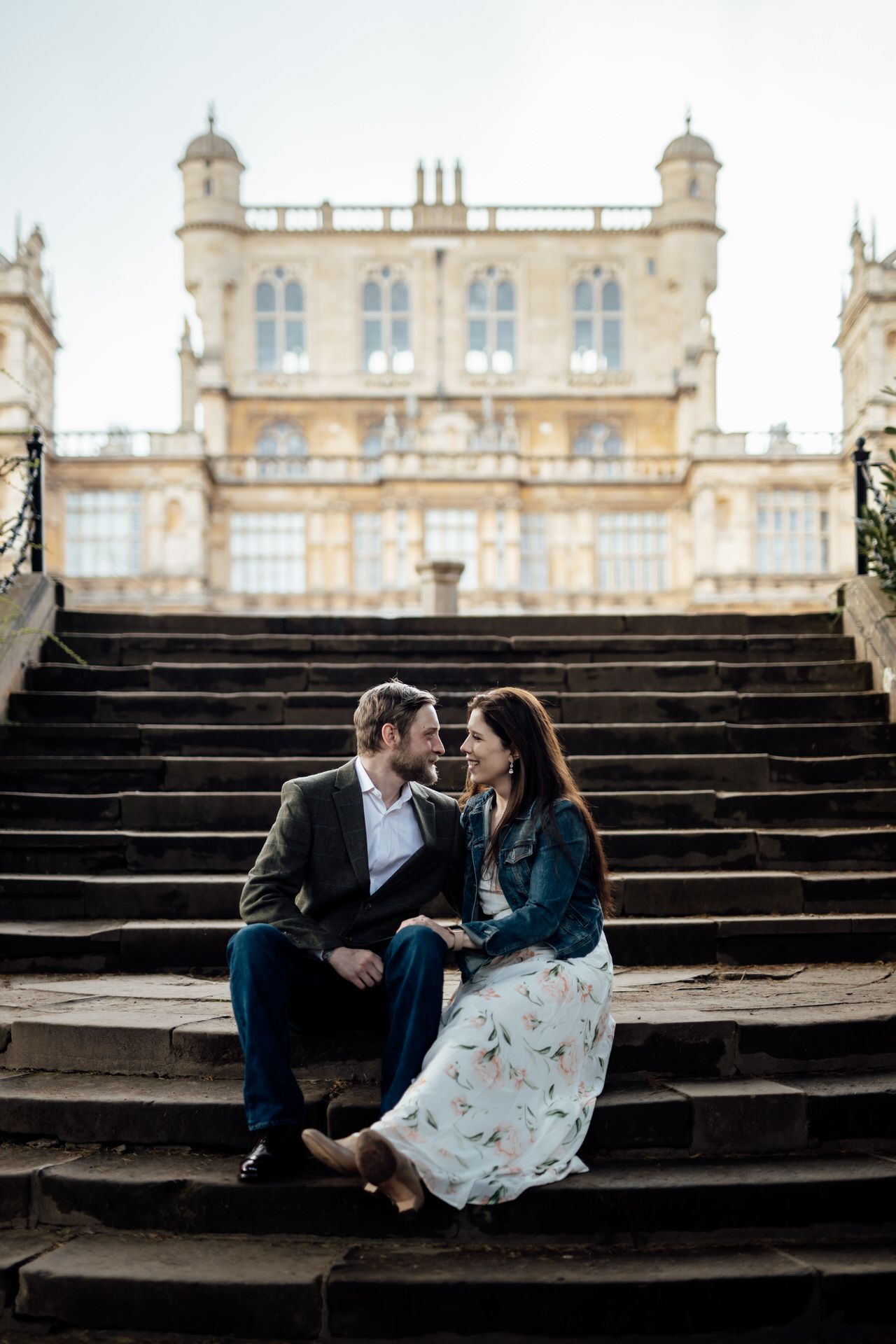 Romantic couple lounging on grand stone steps of historic mansion.