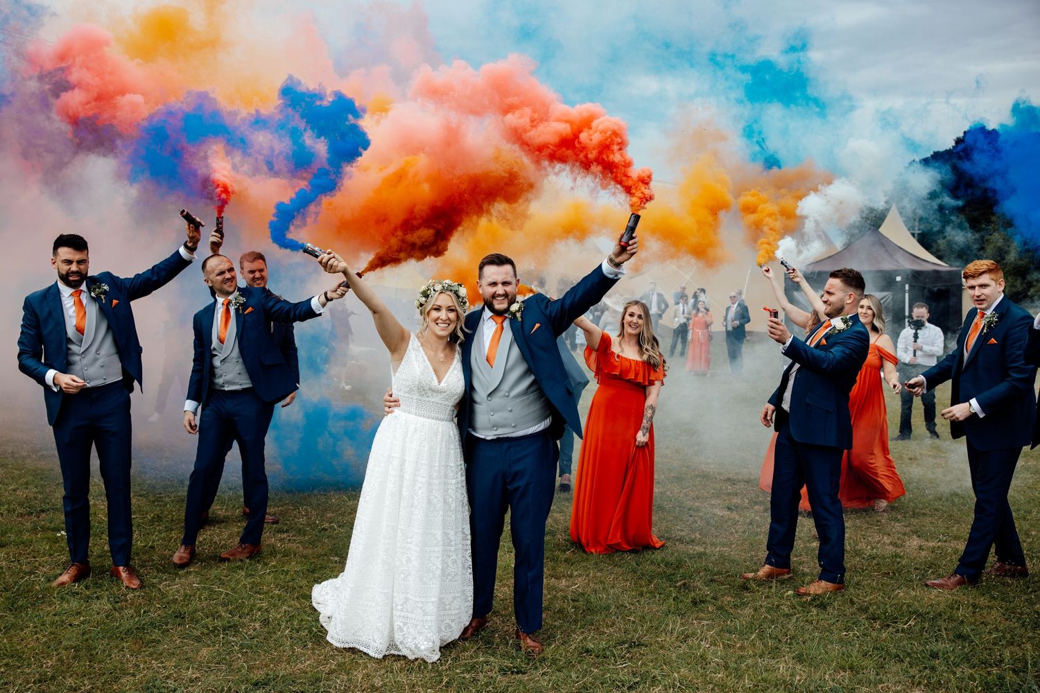 Wedding party celebration with colorful smoke bombs creating vibrant effects outdoors.