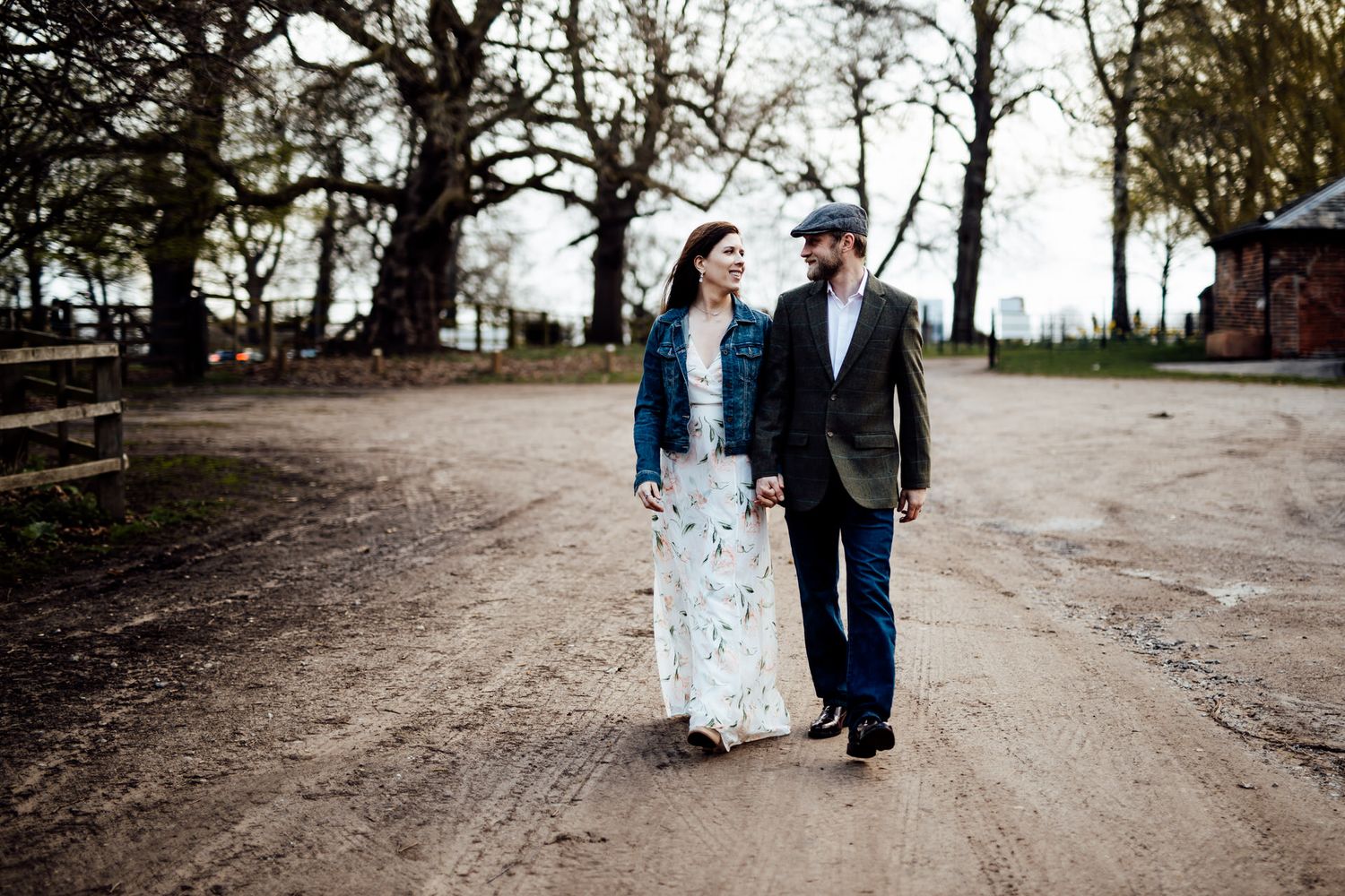 A couple strolls down a scenic dirt path lined with bare trees.