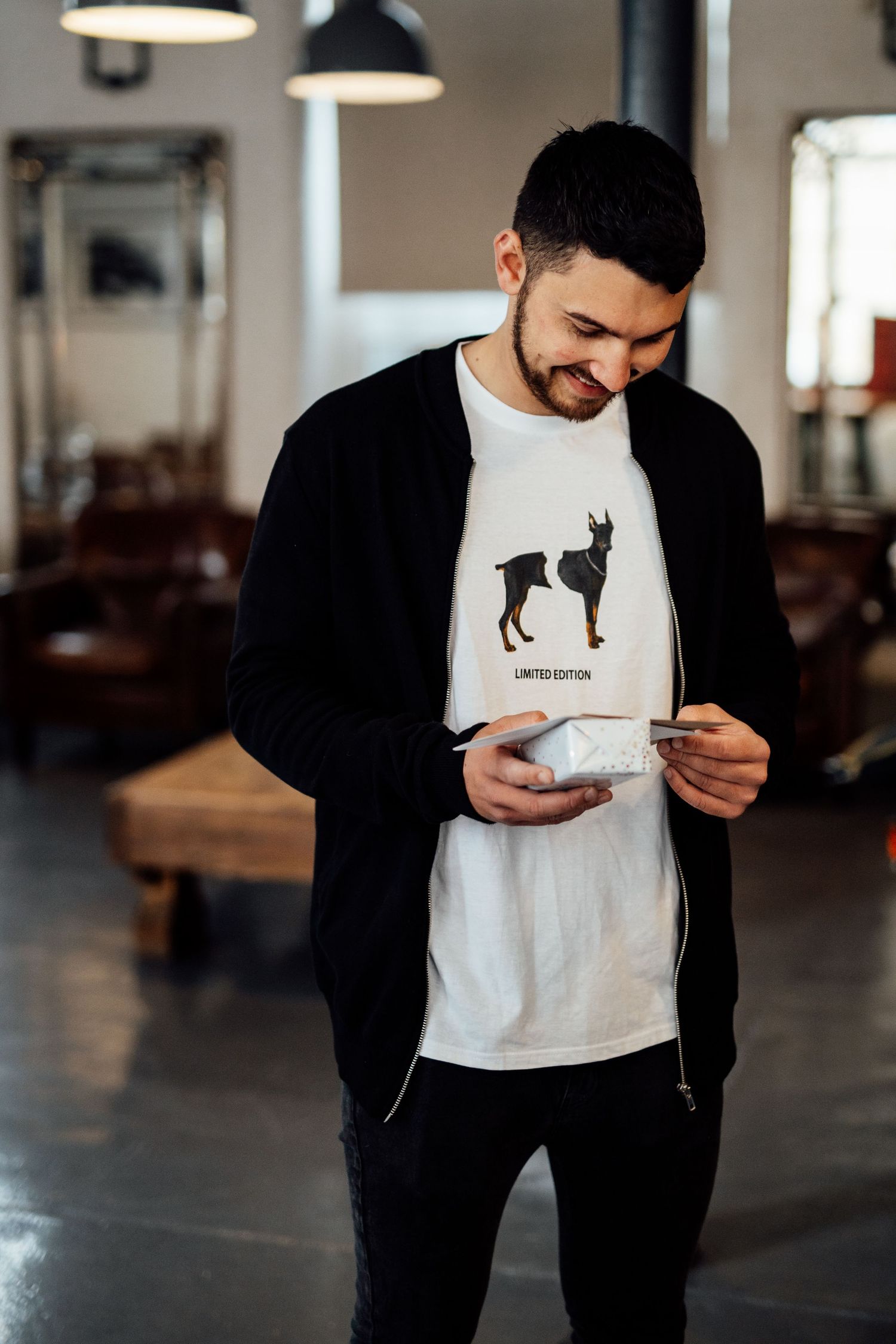 Person wearing black jacket and white t-shirt with dog silhouette design in industrial space.