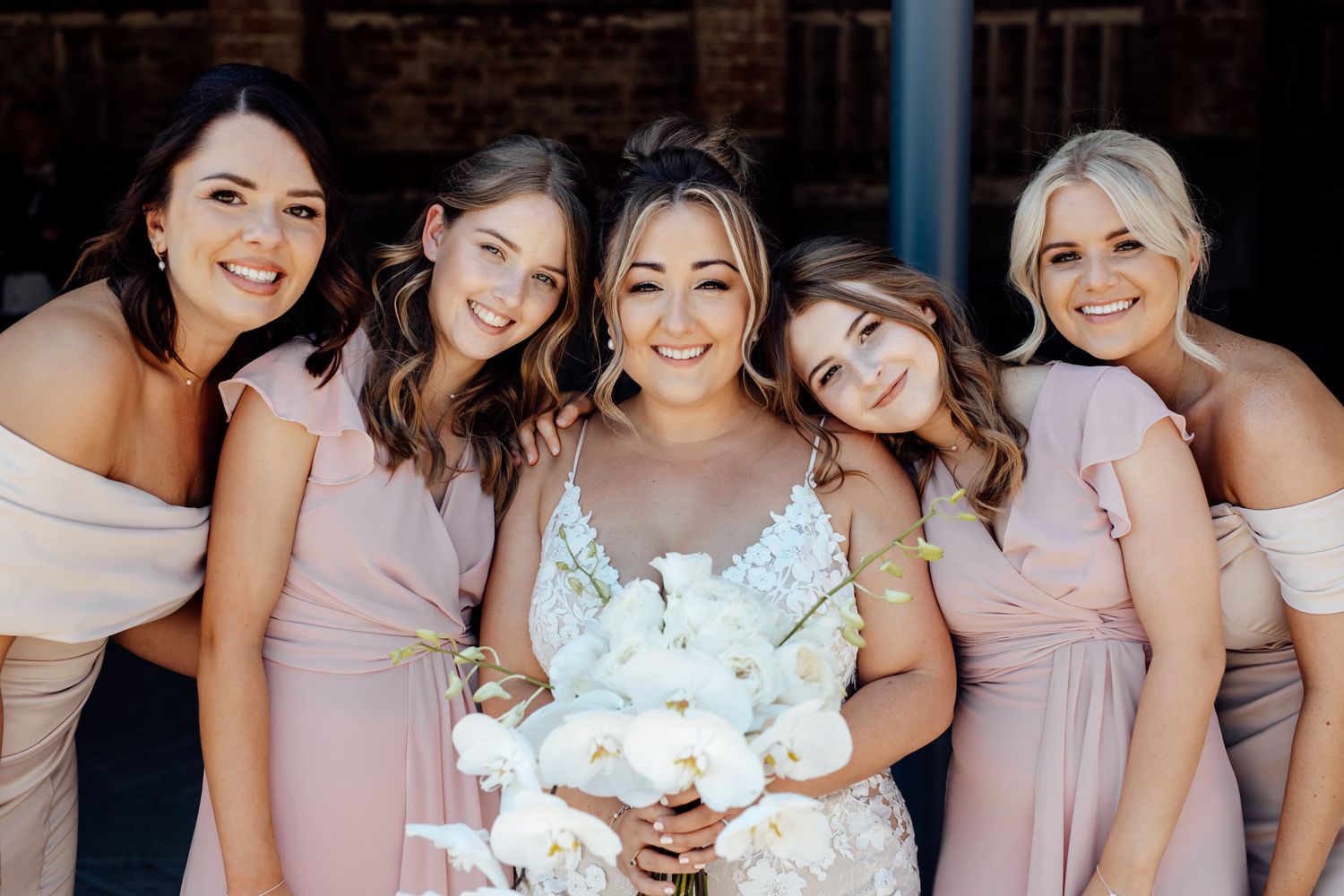 Bridesmaids in blush pink dresses posing together at wedding venue.