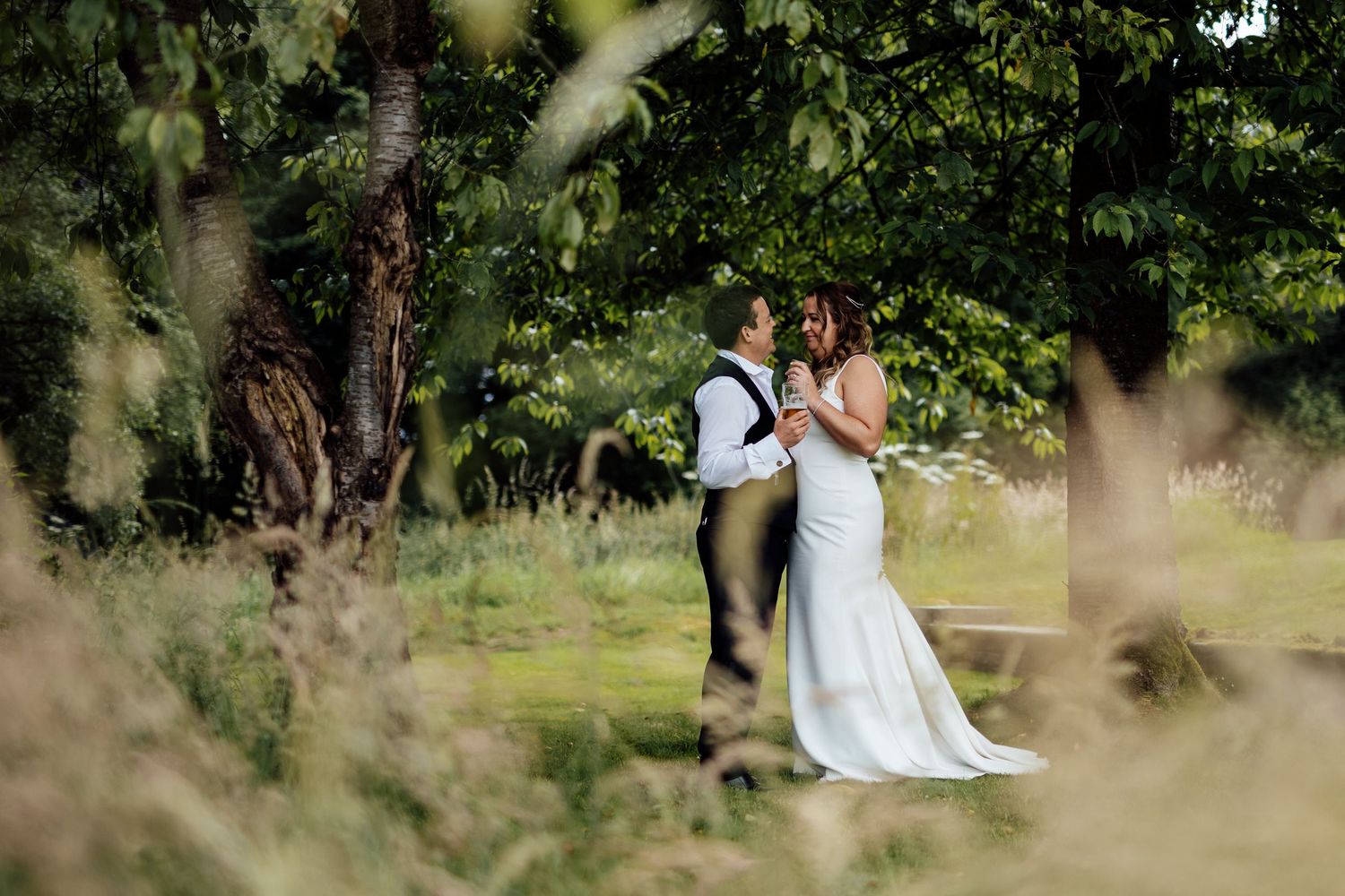 Wedding couple photographed through tall grass in a natural outdoor setting.