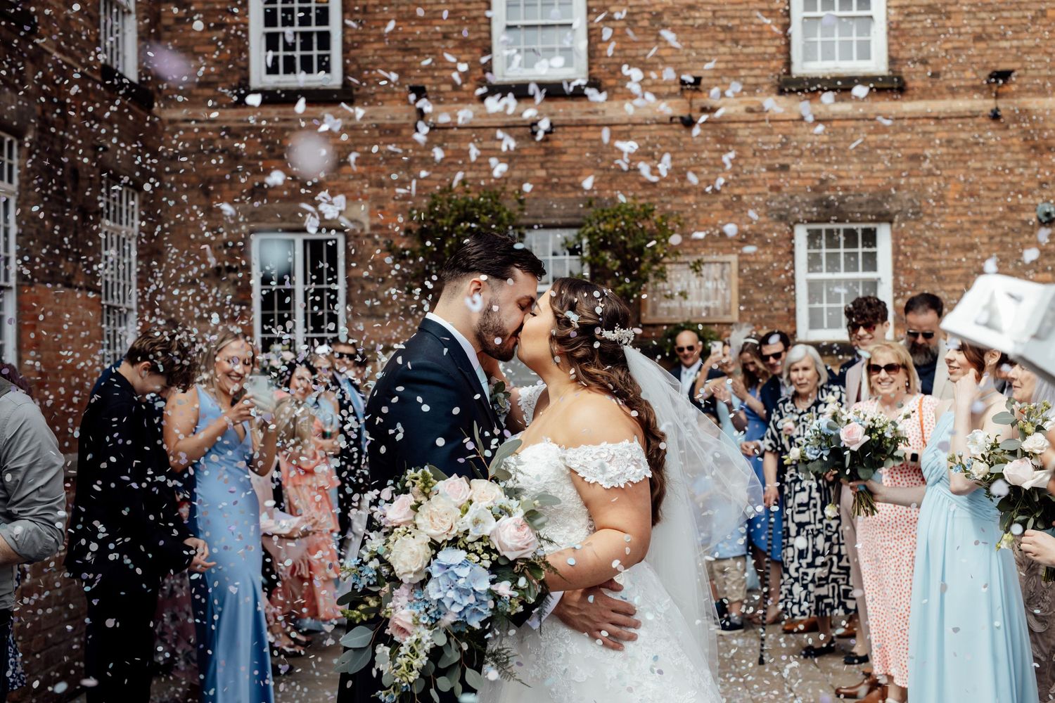 Wedding party celebration with confetti outside historic brick building.