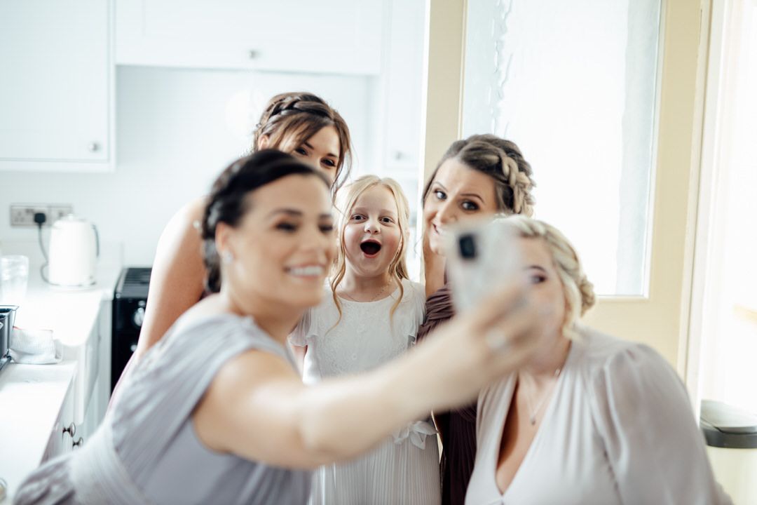 Bridesmaids in soft pink dresses share joyful laughter while getting ready for a wedding celebration.