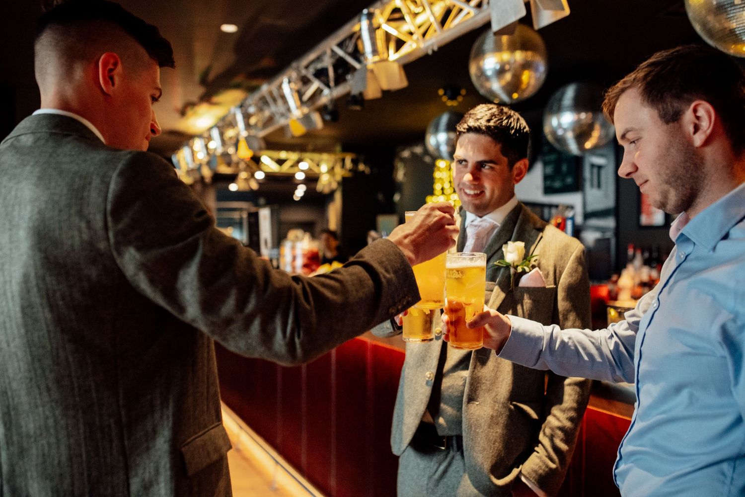 Wedding guests enjoying drinks and conversation at wooden bar counter.