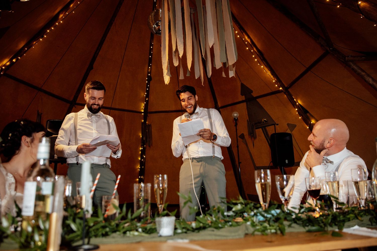 Reception celebration inside a rustic tent venue with string lights and greenery decor.
