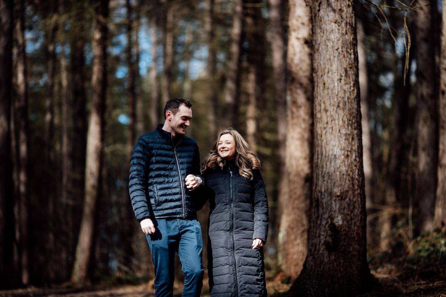 Romantic couple in puffy winter jackets walking together through a pine forest.